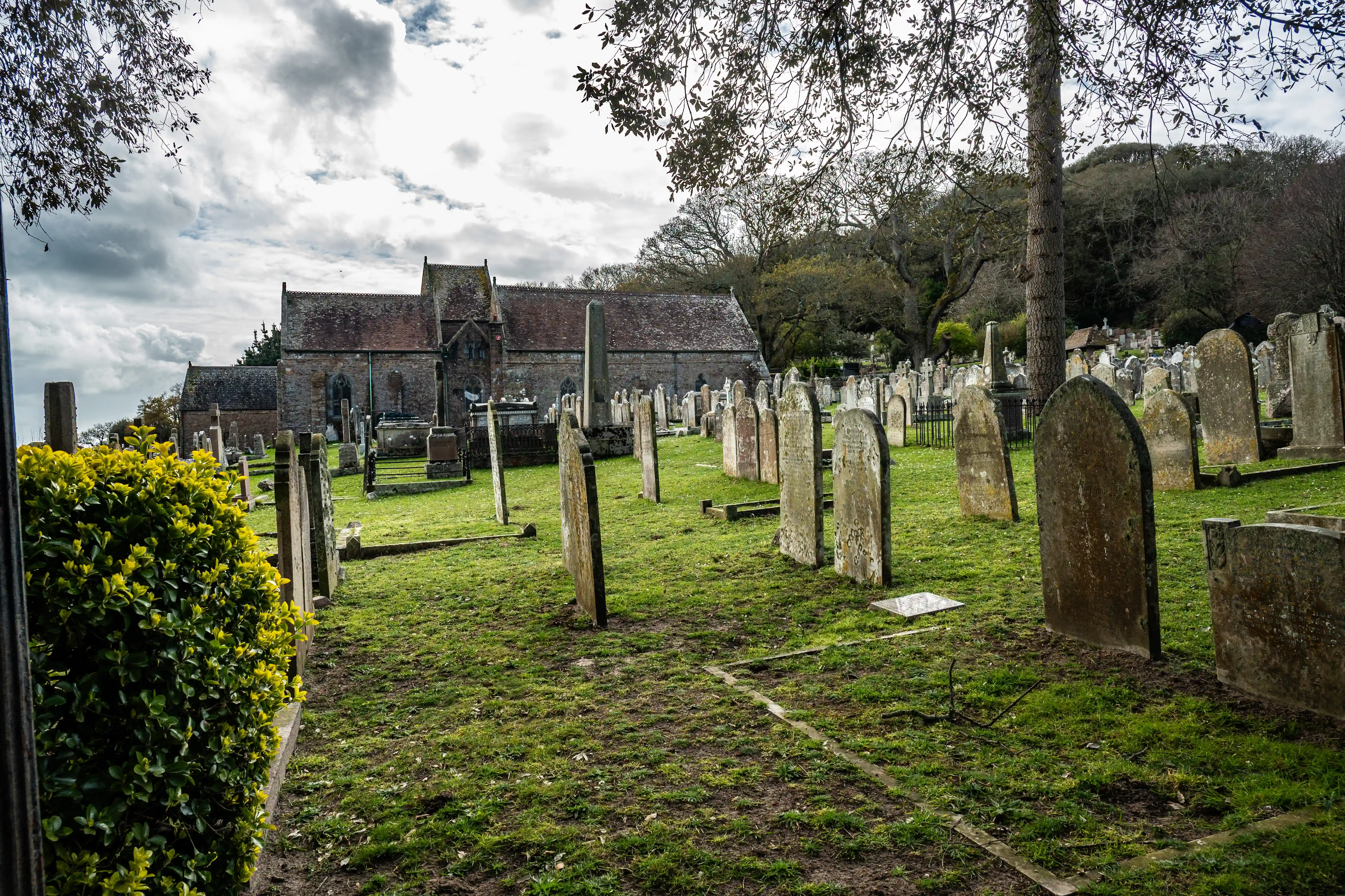 A cemetery with many old gravestones and a stone church in the background on a cloudy day.