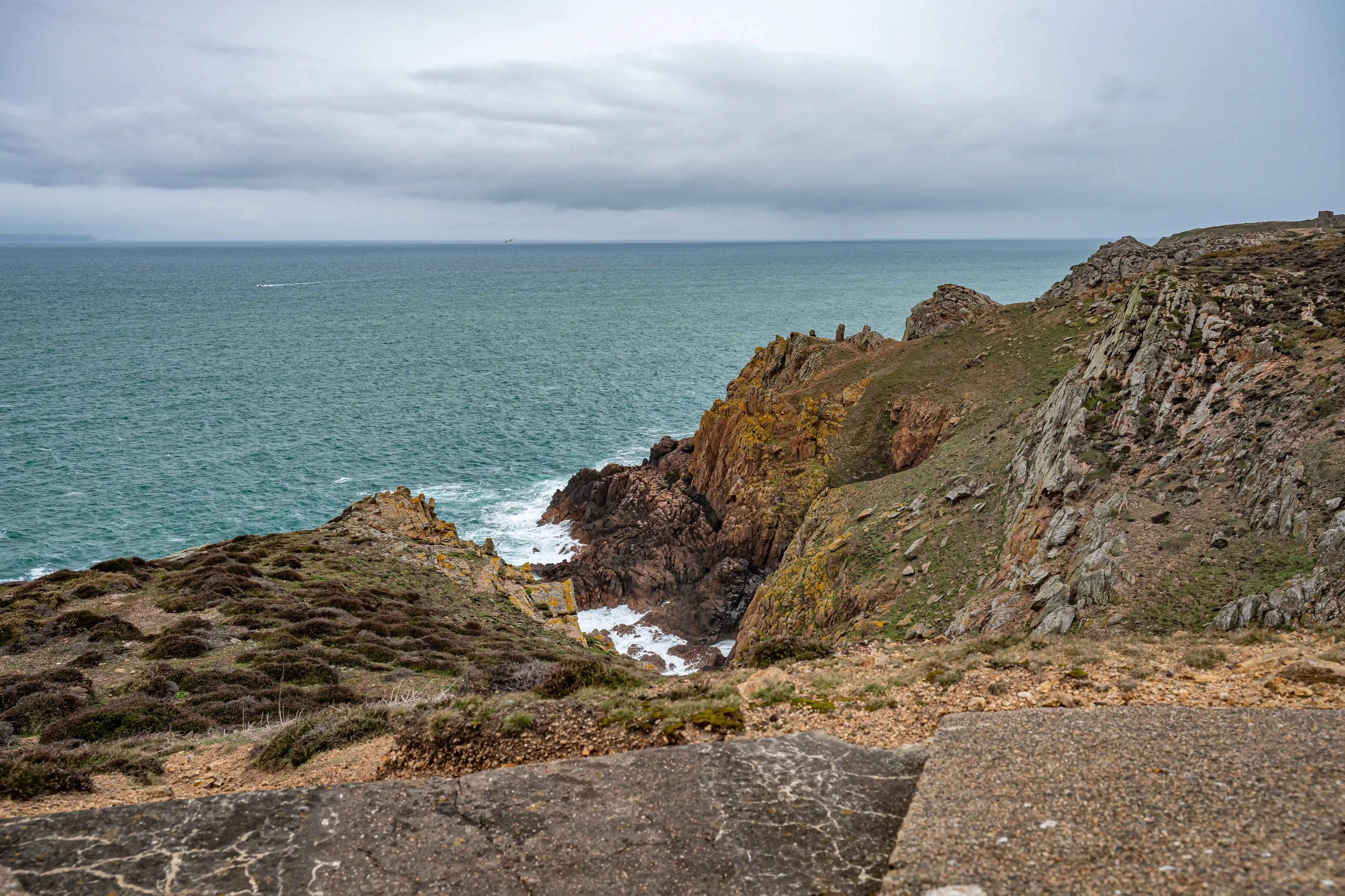 Overcast view of a rugged, rocky coastline in Cornwall, with the sea on the left and a concrete foreground.