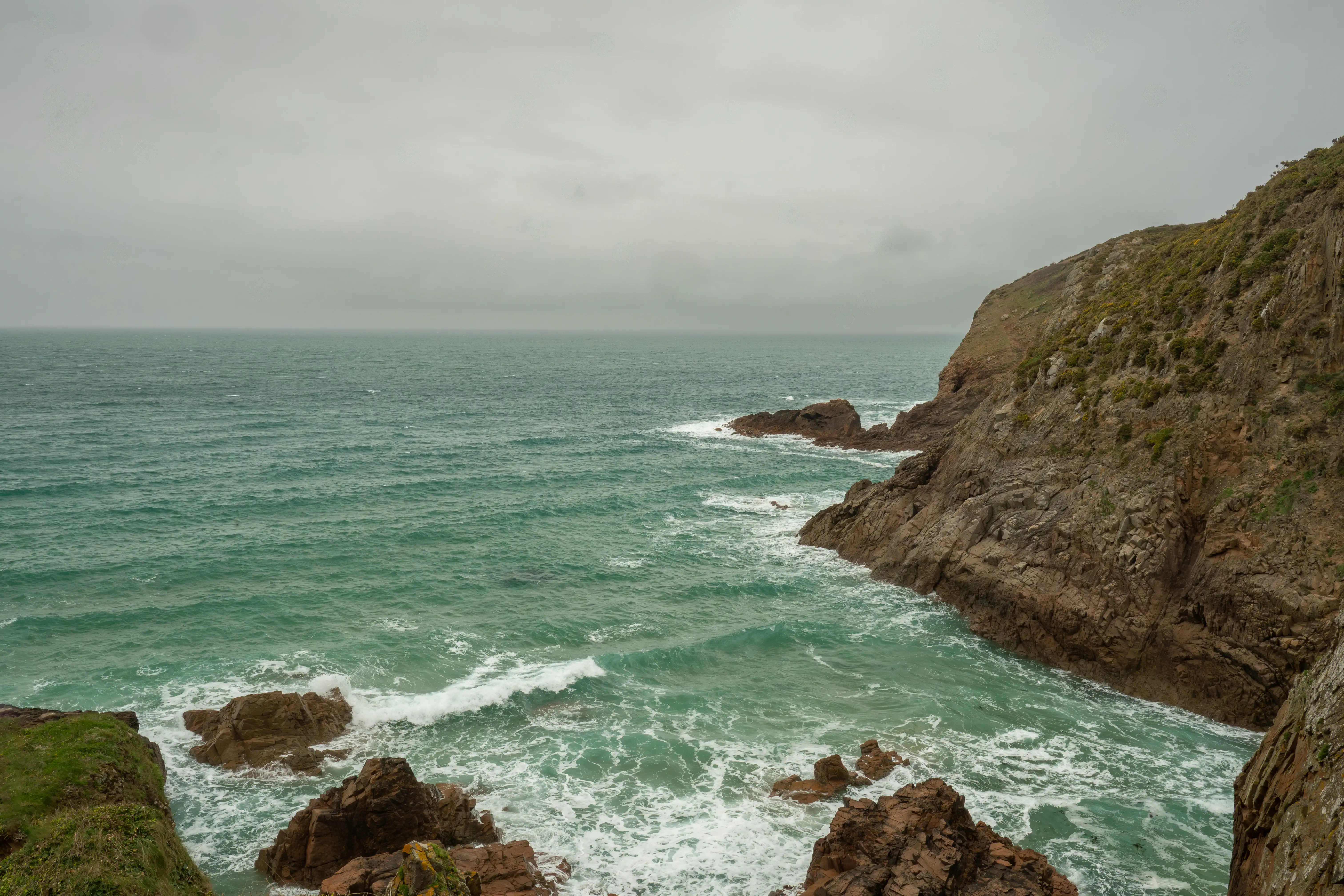 A wide shot of a rocky coastline with green sea and a cloudy sky.
