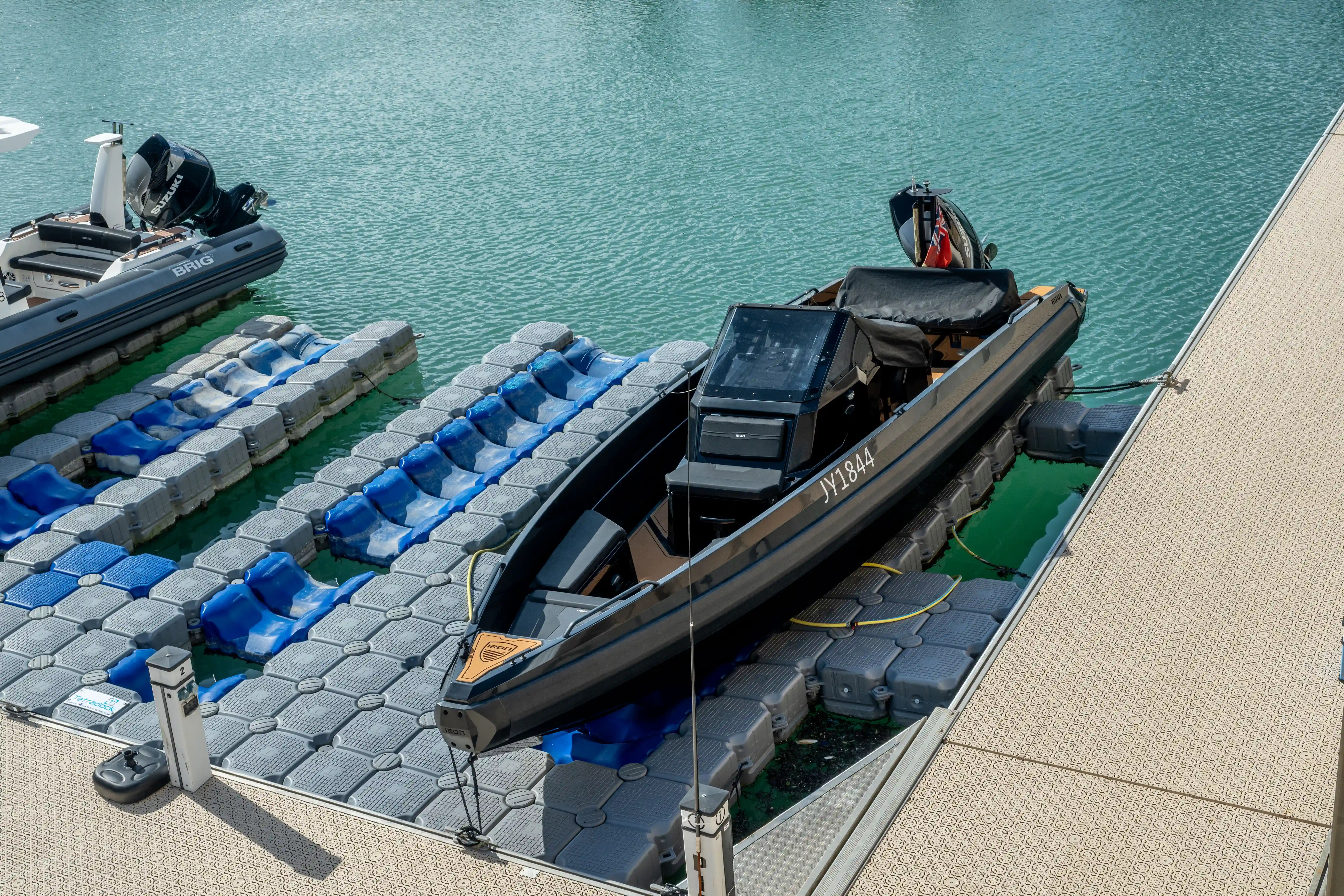 Two modern inflatable boats are docked side-by-side on a floating pontoon system in calm, clear turquoise water, viewed from above.
