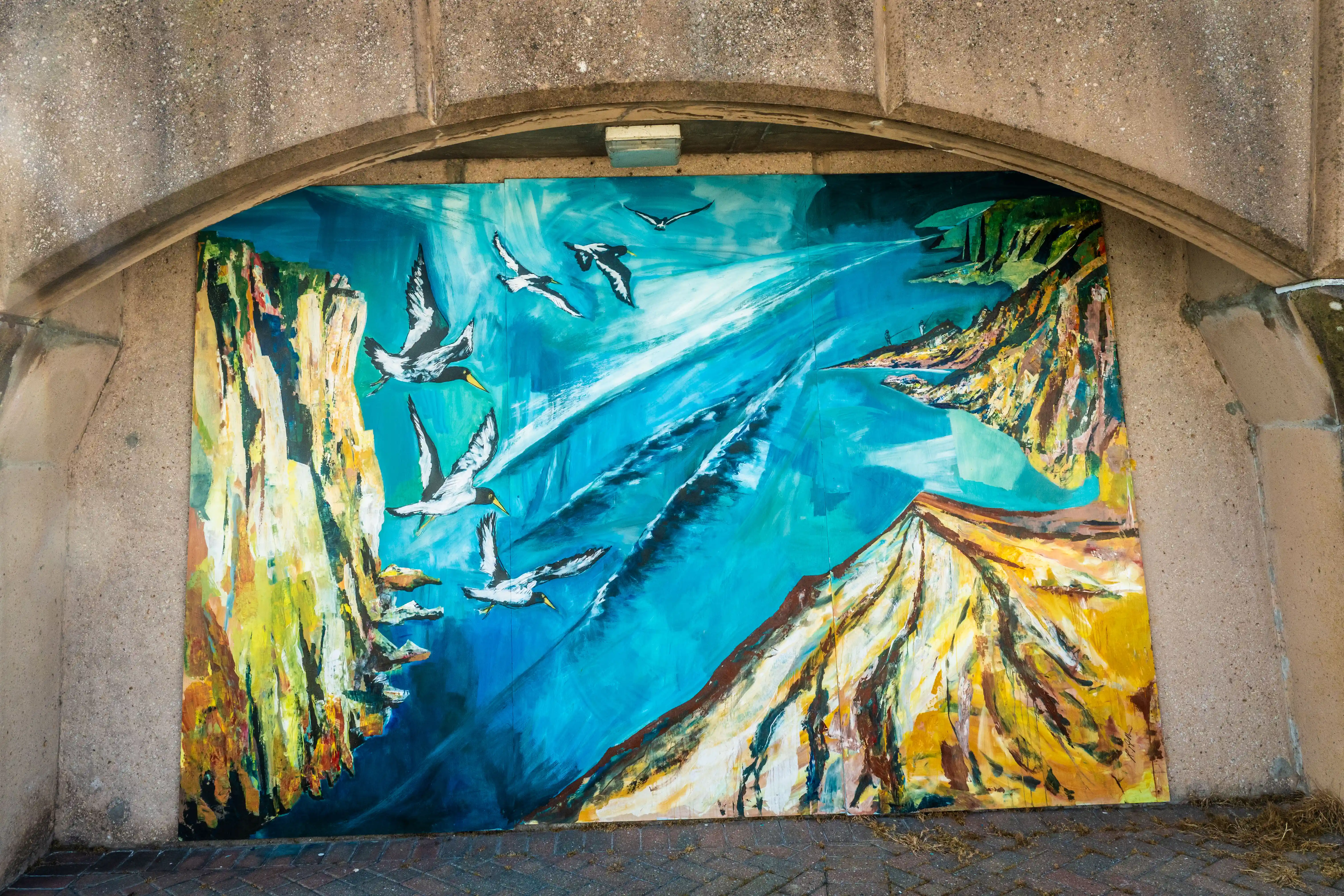 A colourful mural of seabirds flying over cliffs under a concrete archway.