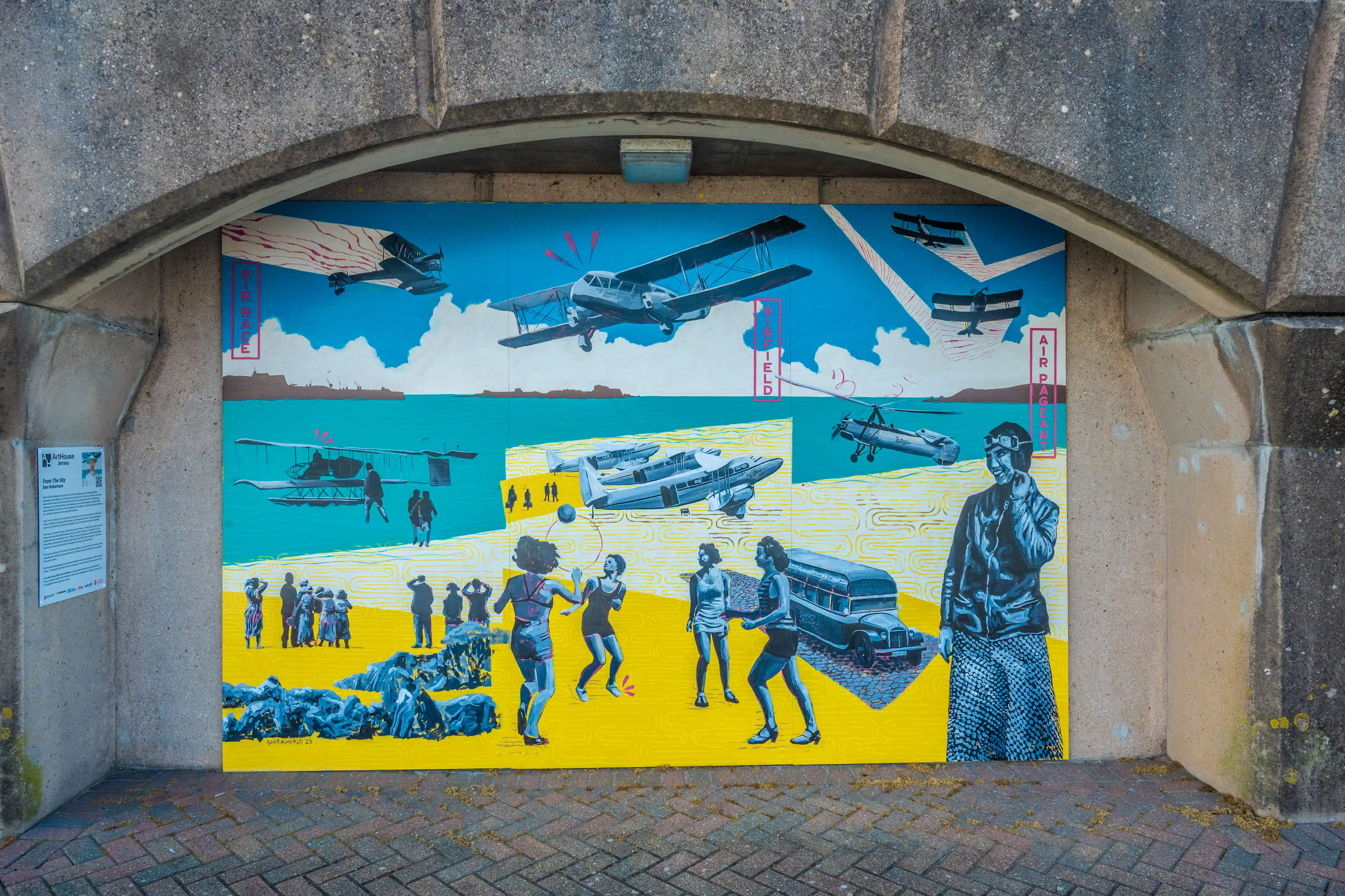 Mural depicting vintage airplanes flying above people on a yellow ground, beneath a concrete bridge. A pilot in goggles smiles towards the viewer on the right side.