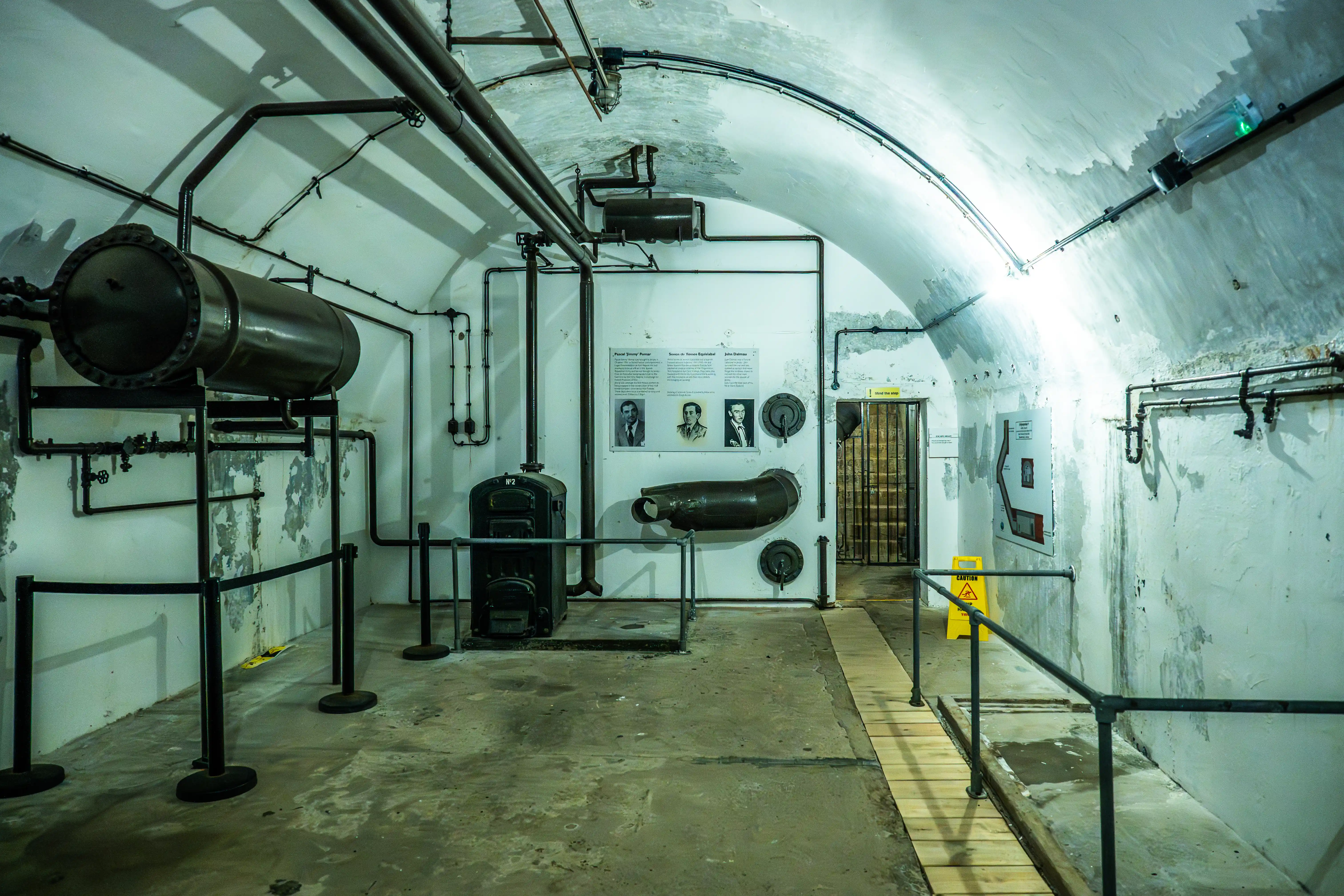 Interior of an underground bunker with pipes, machinery, and display boards.