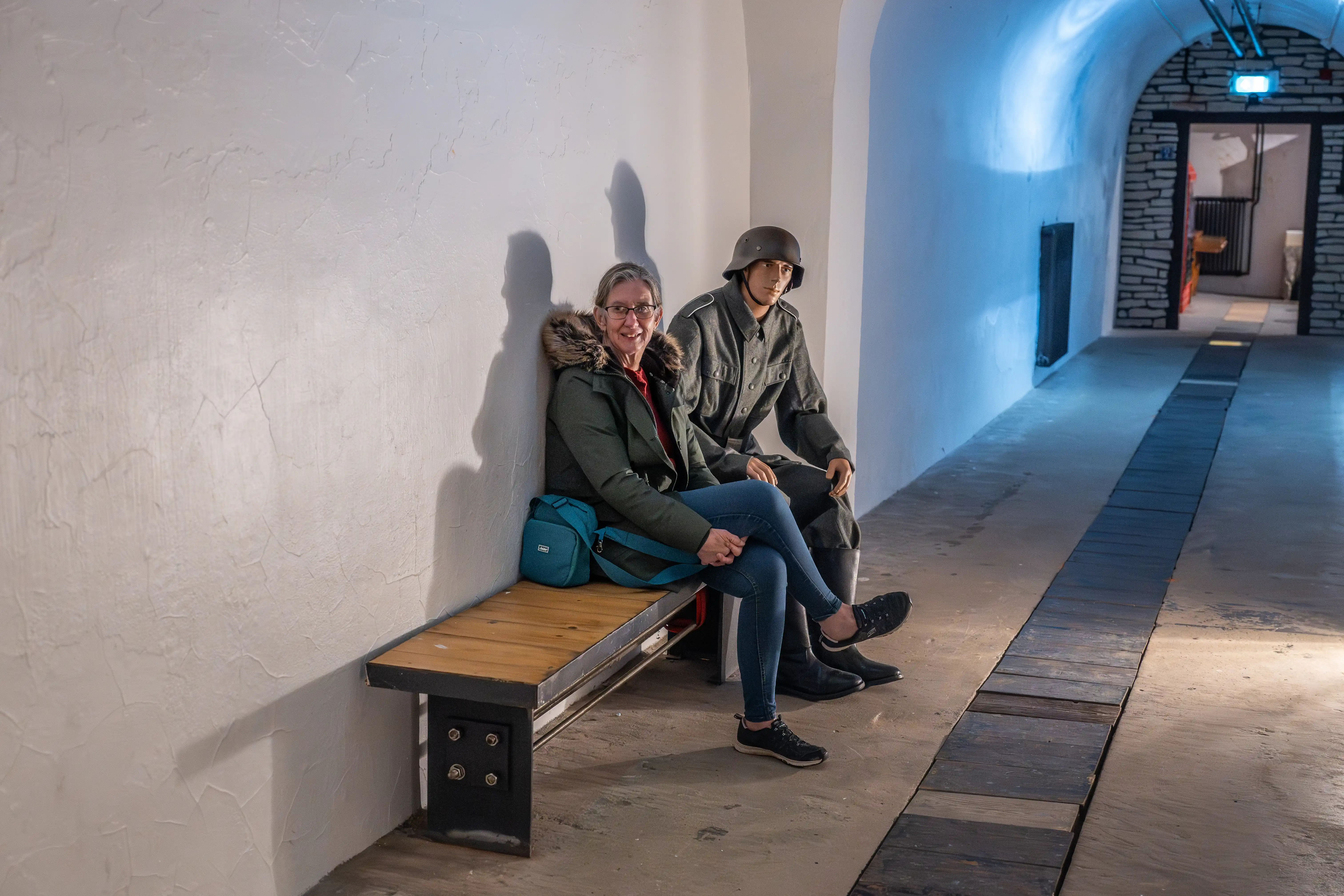 A woman sits on a bench next to a mannequin wearing a historical military uniform inside a tunnel.