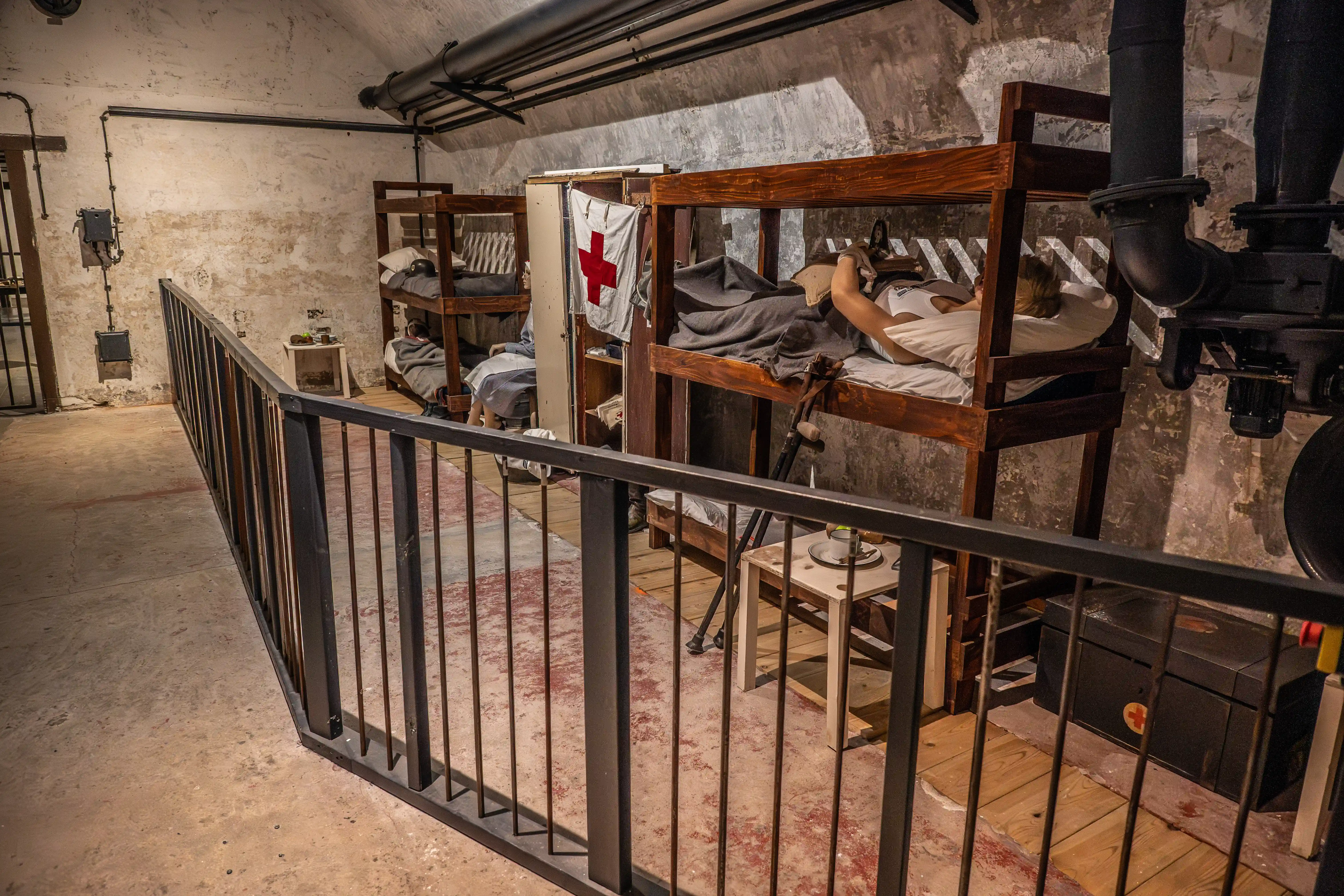 A dimly lit, historical ward interior with multiple wooden bunk beds, a Red Cross flag, and a figure resting in one of the beds.