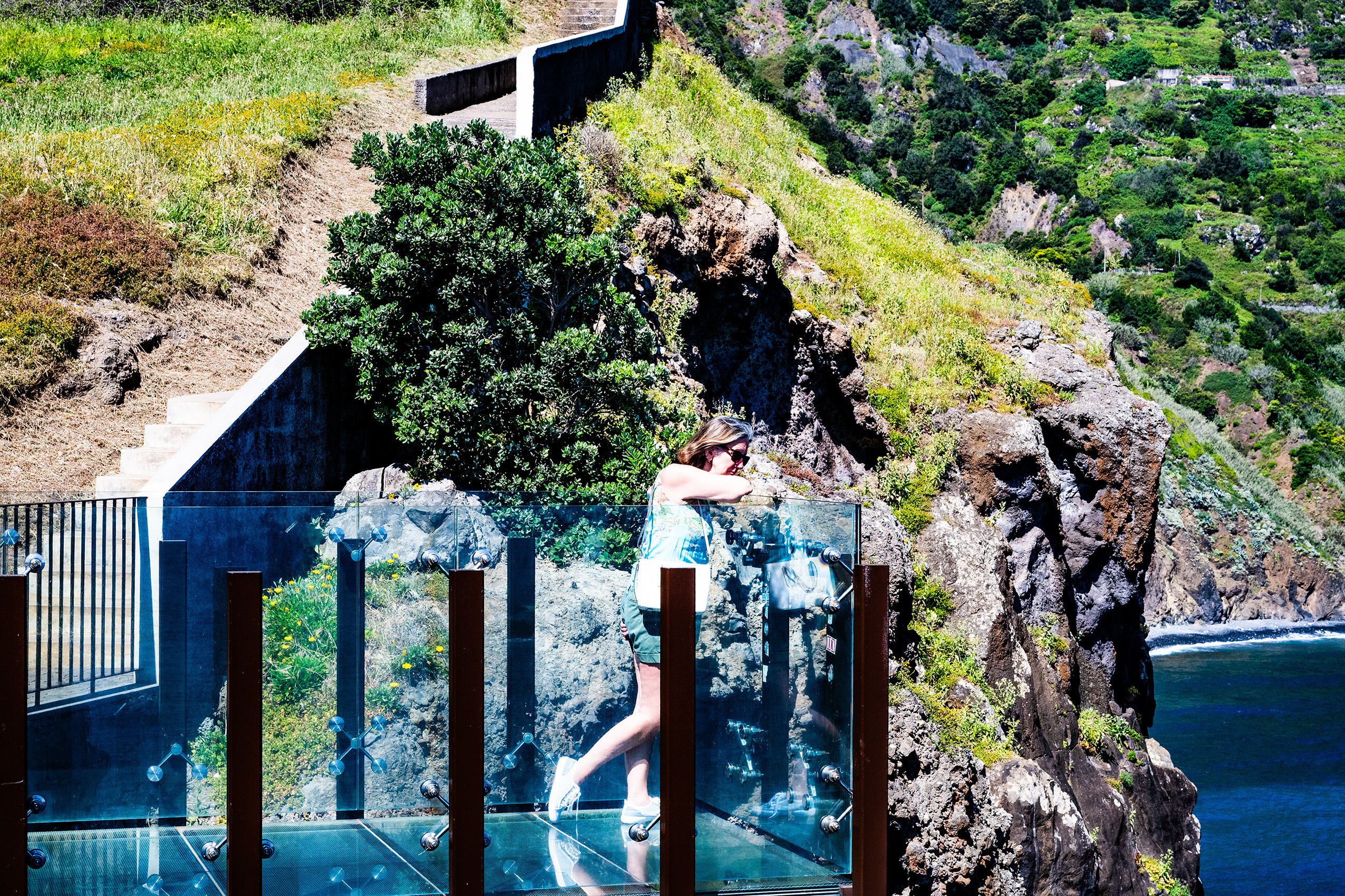 person standing on a glass-bottomed observation deck that extends over a cliff