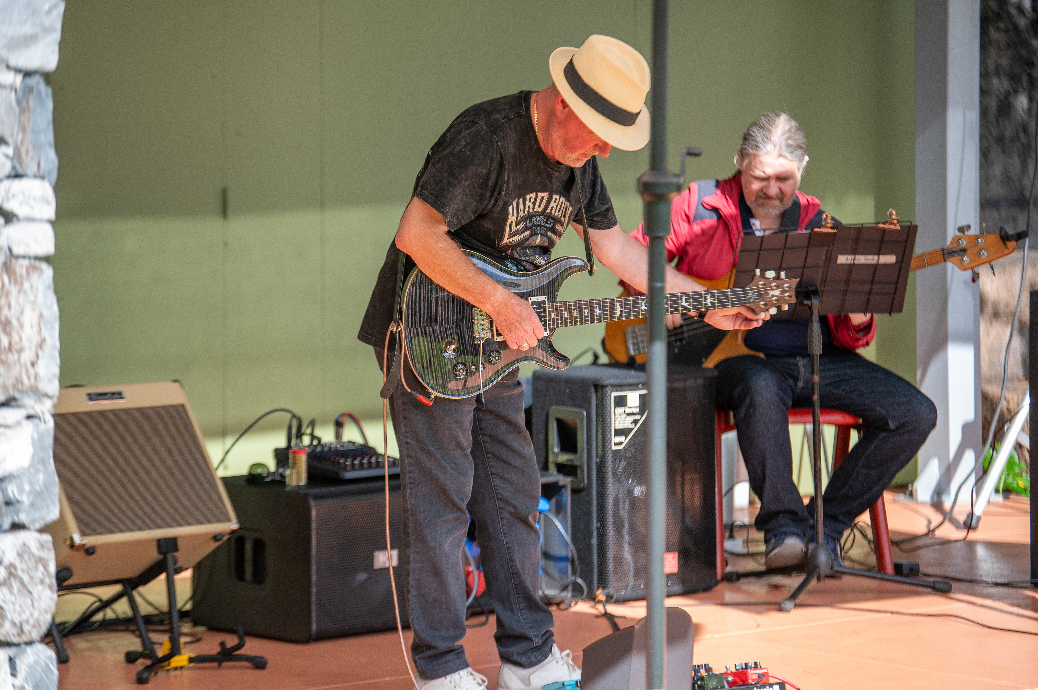 The musician on the left, wearing a hat and a black t-shirt, is playing an electric guitar