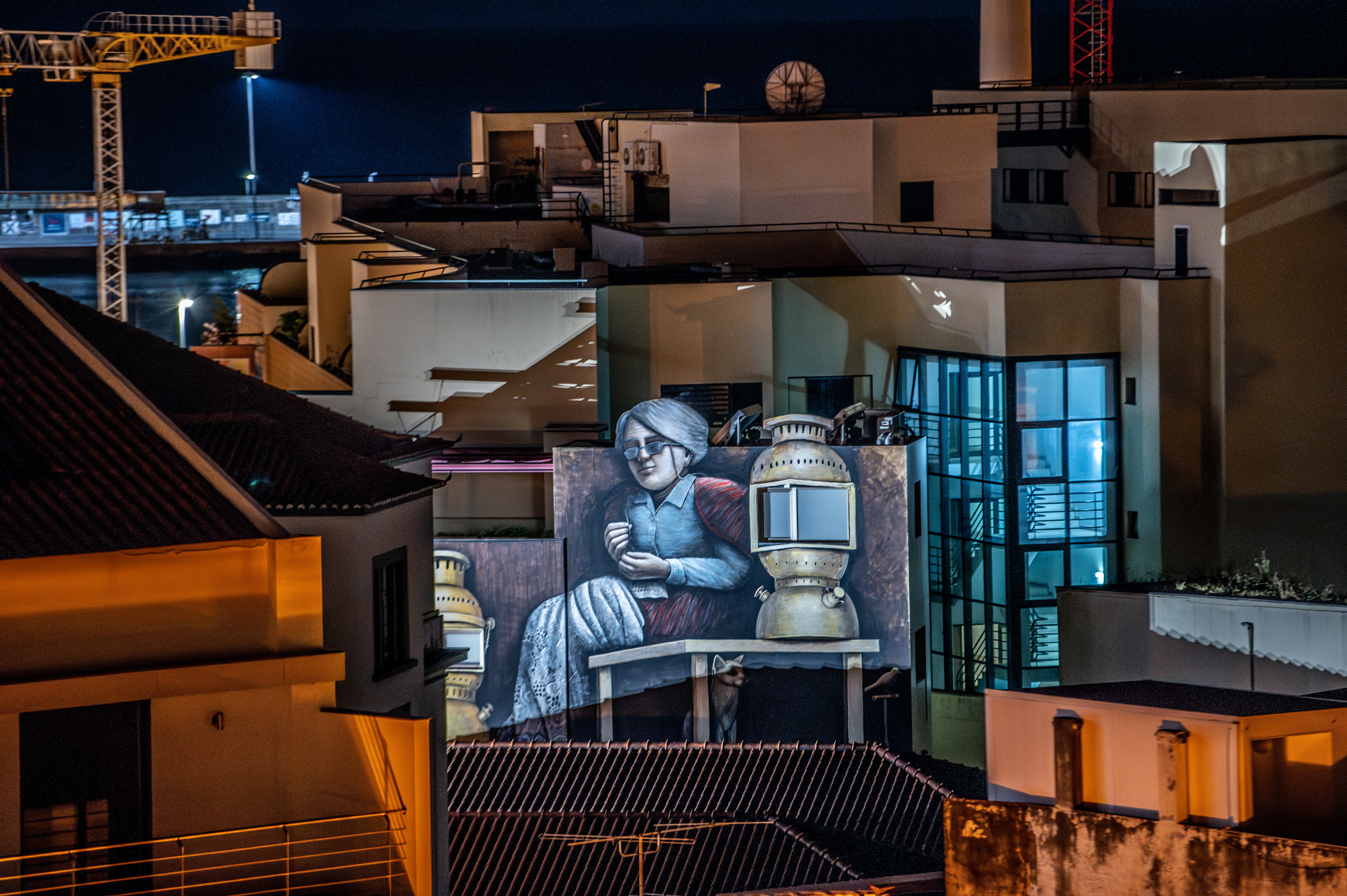 nighttime urban scene featuring a mural on the side of a building