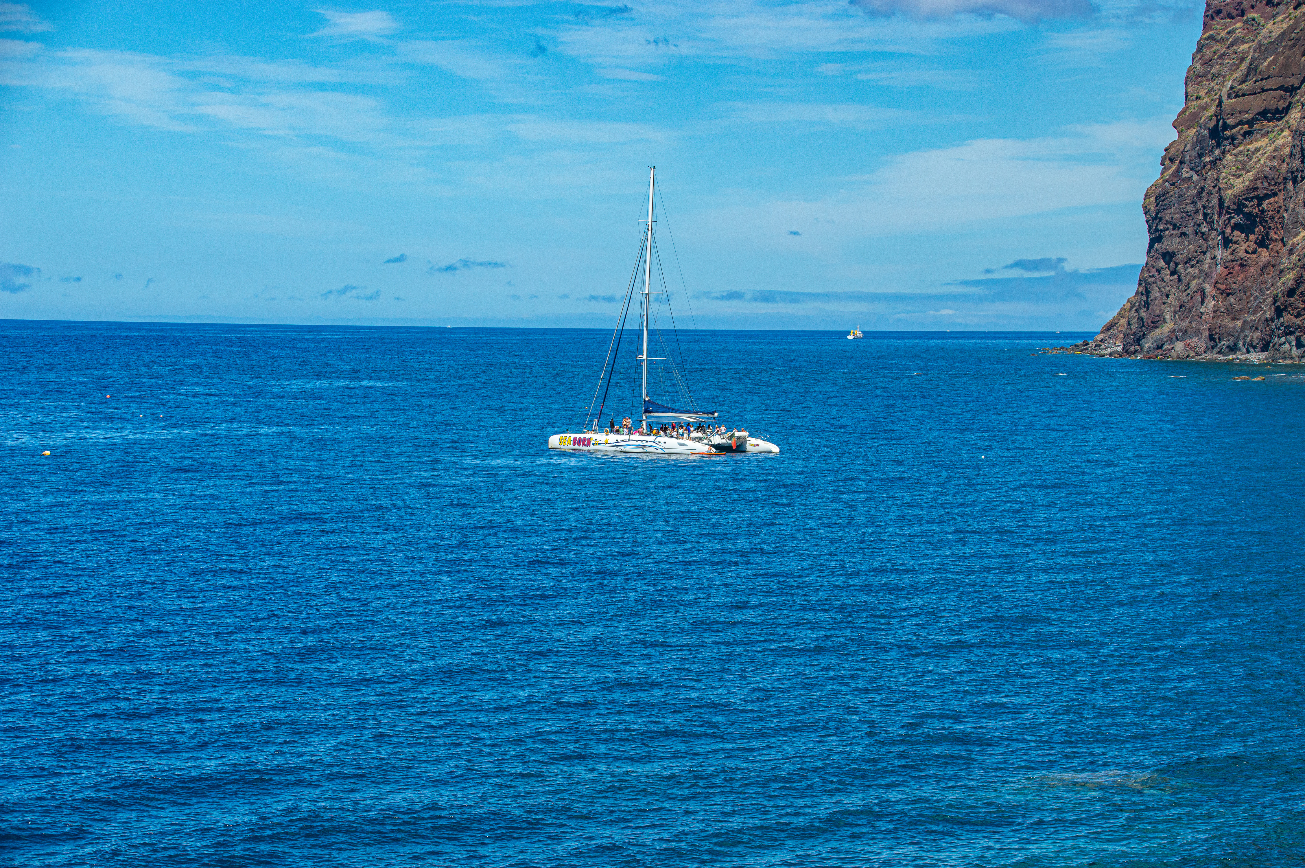 catamaran sailing near a rocky coastline