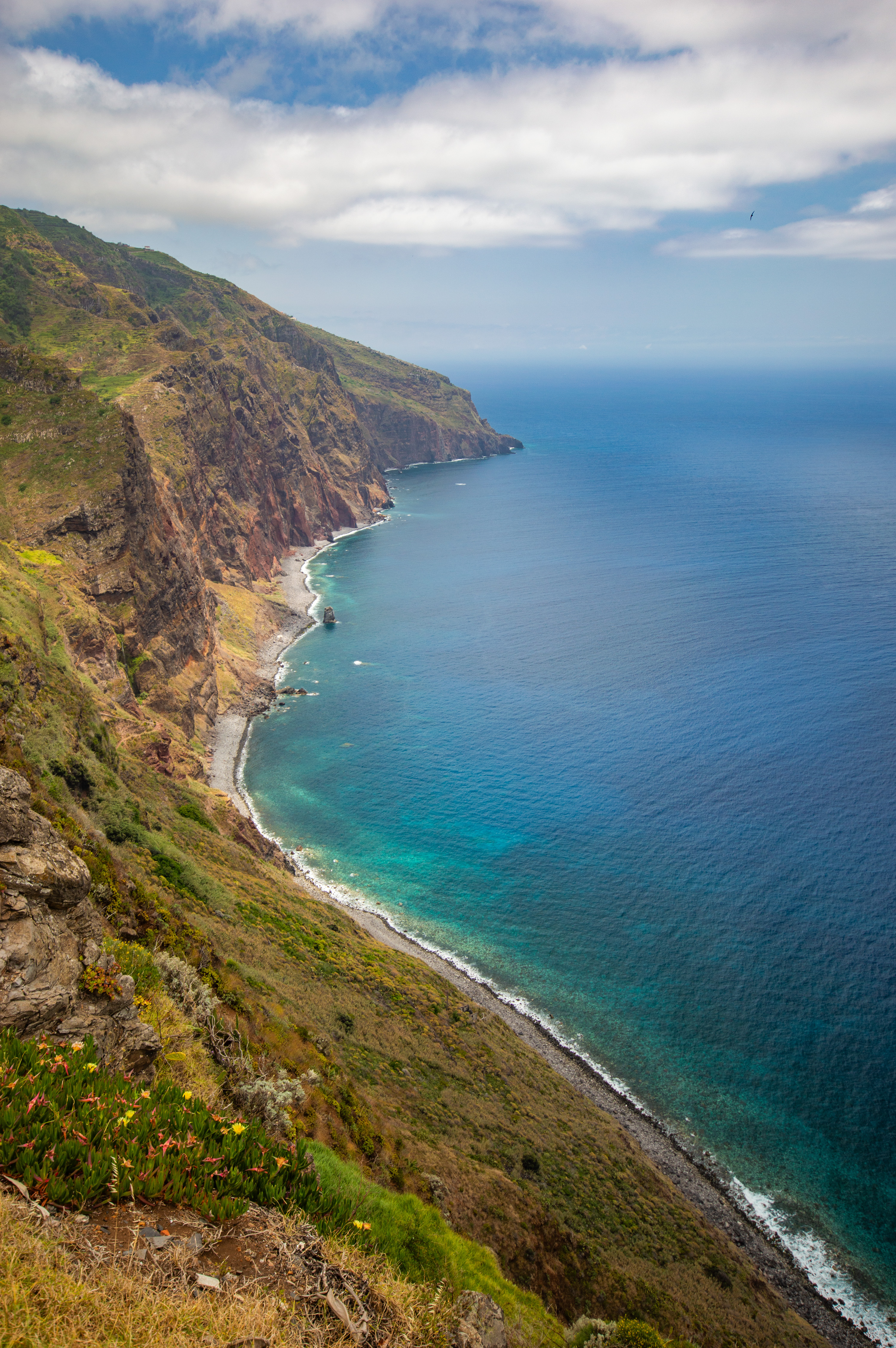 The cliff descends to a narrow beach with clear, turquoise water