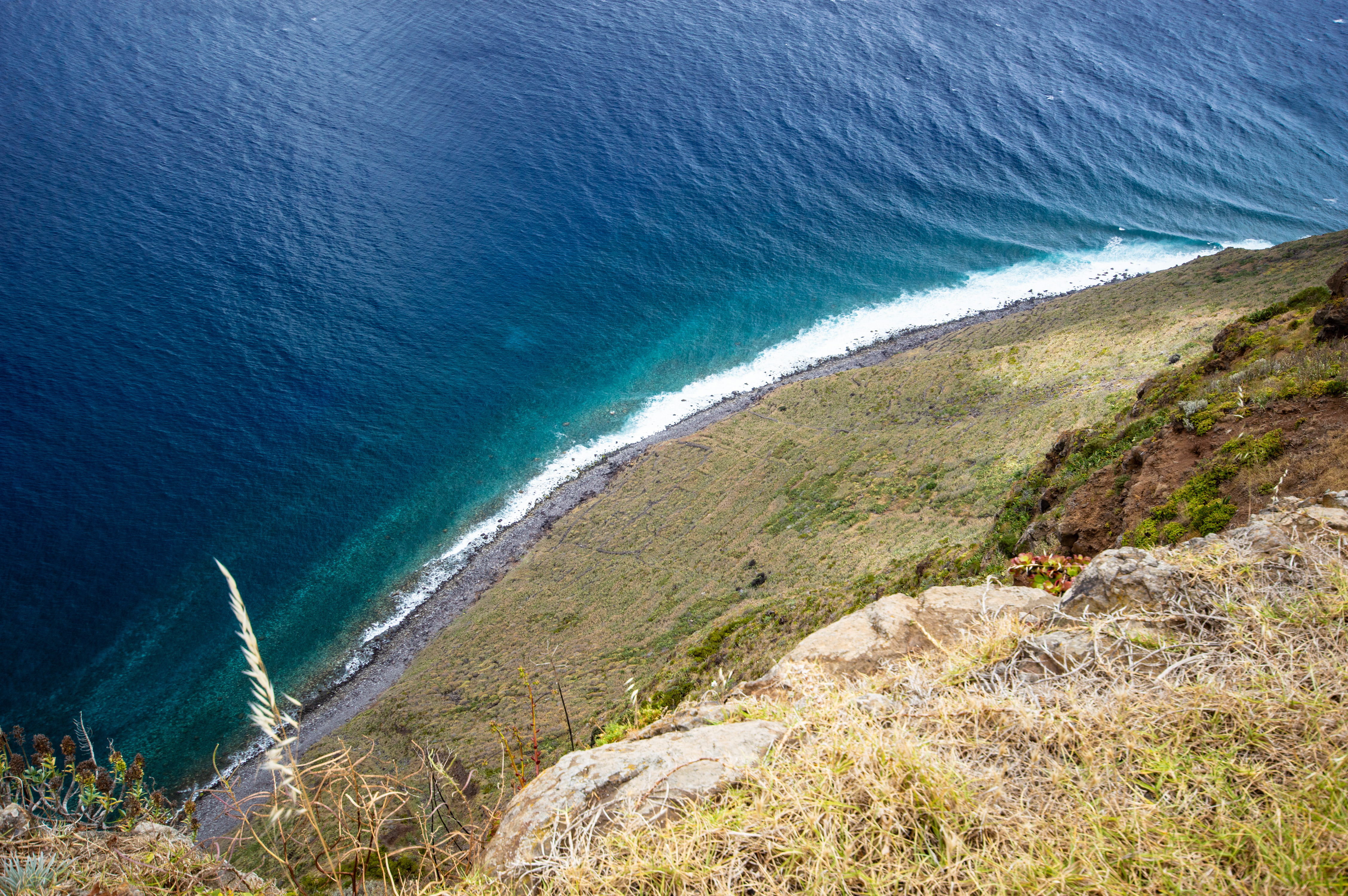 water is a deep blue, with waves crashing against the base of the cliff