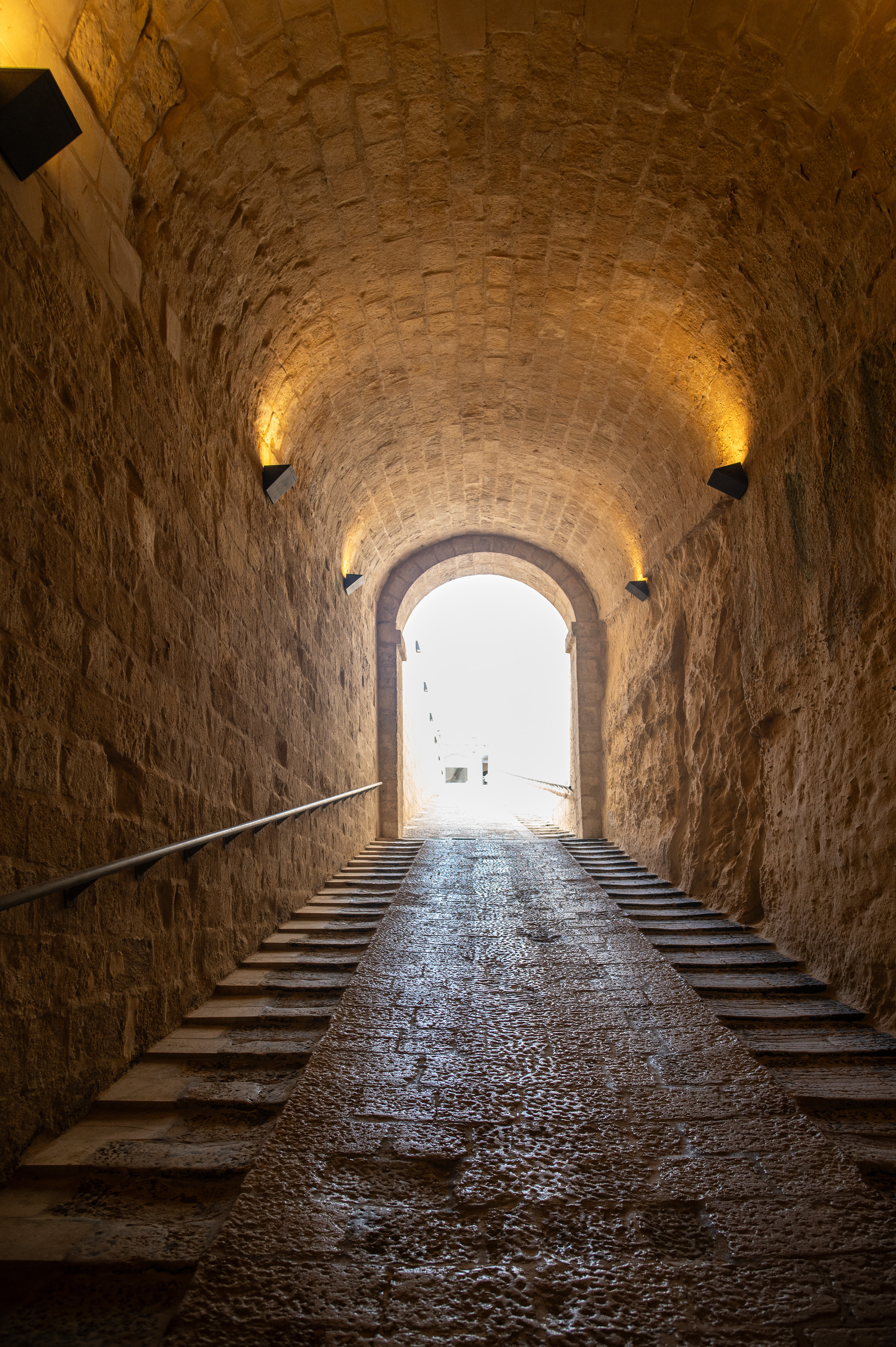tunnel with stone walls and a cobblestone path leading upwards to a bright exit