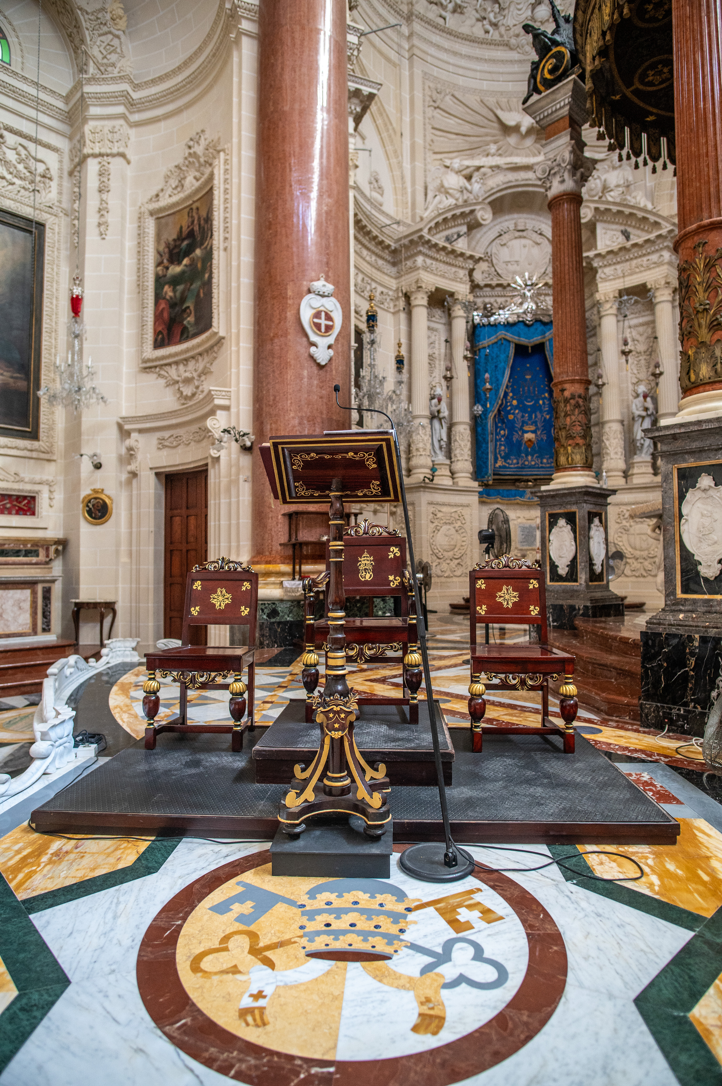 a lectern with a microphone, two smaller chairs, and a central throne-like chair