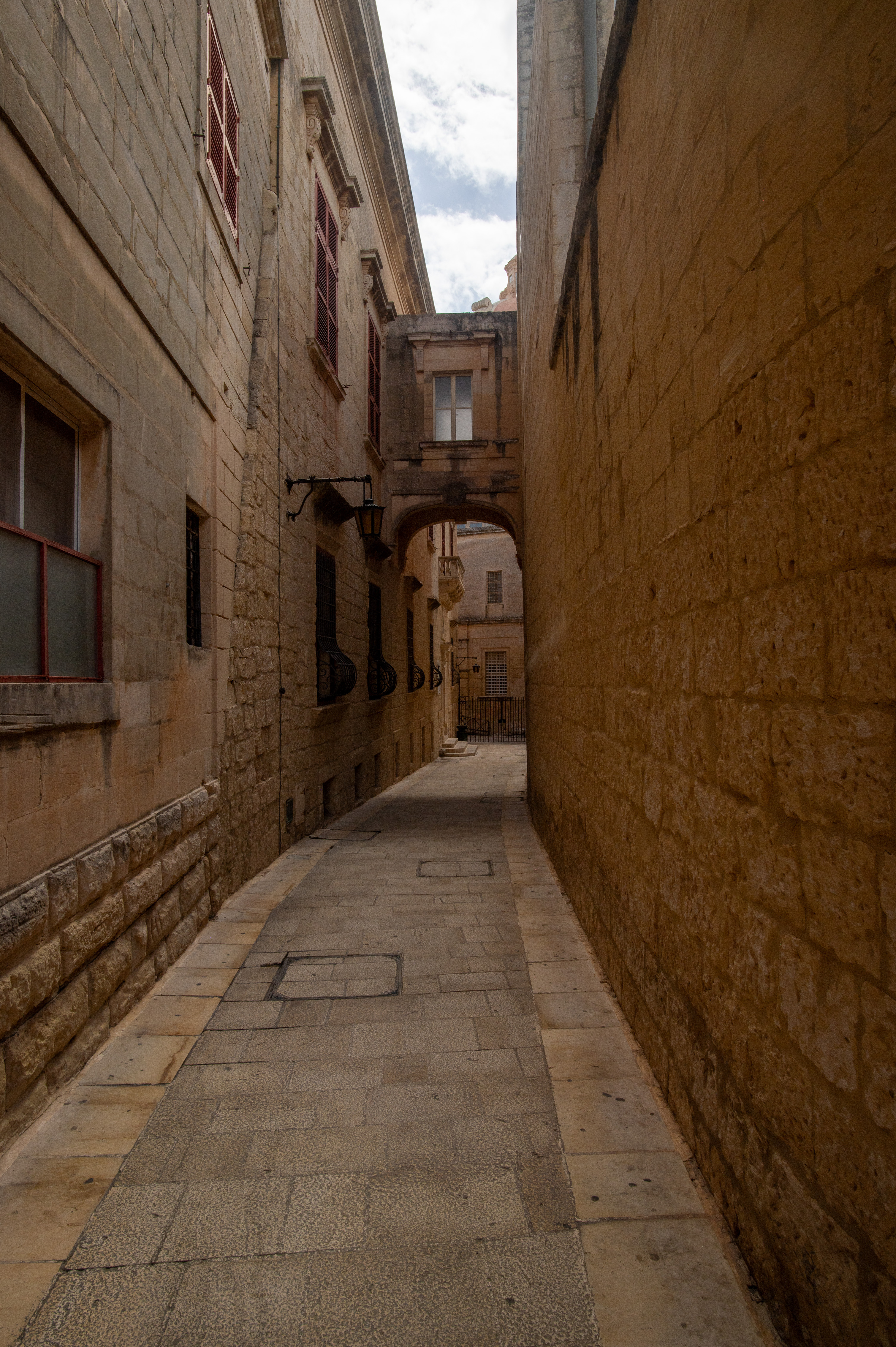 a narrow, stone-paved alleyway flanked by tall, beige stone buildings