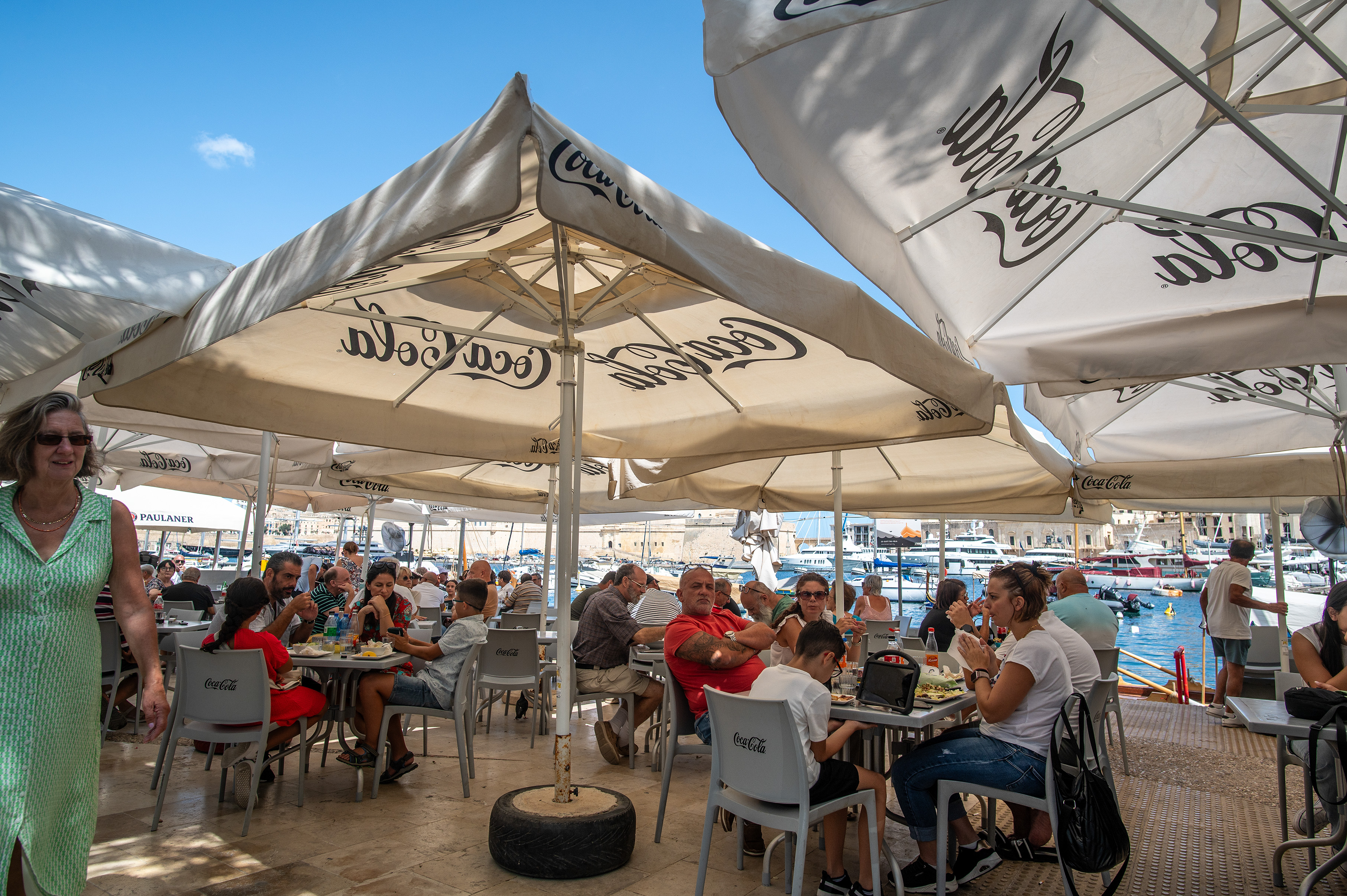Several groups of people are seated at tables under large umbrellas
