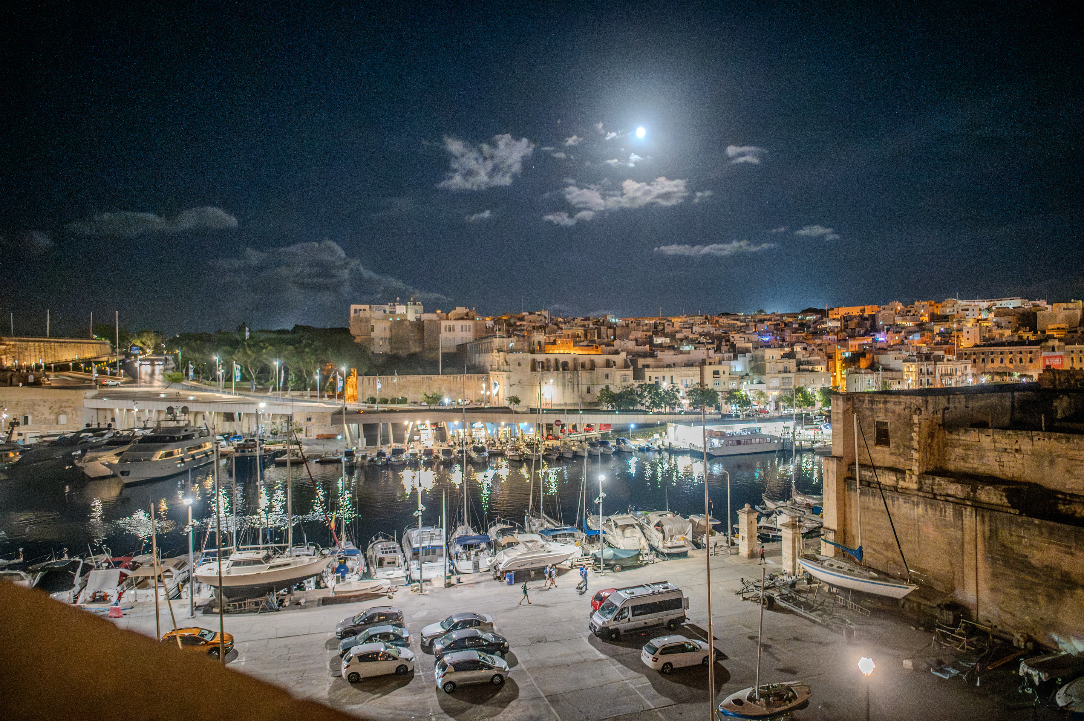 a nighttime scene of a harbor with boats docked and a cityscape in the background