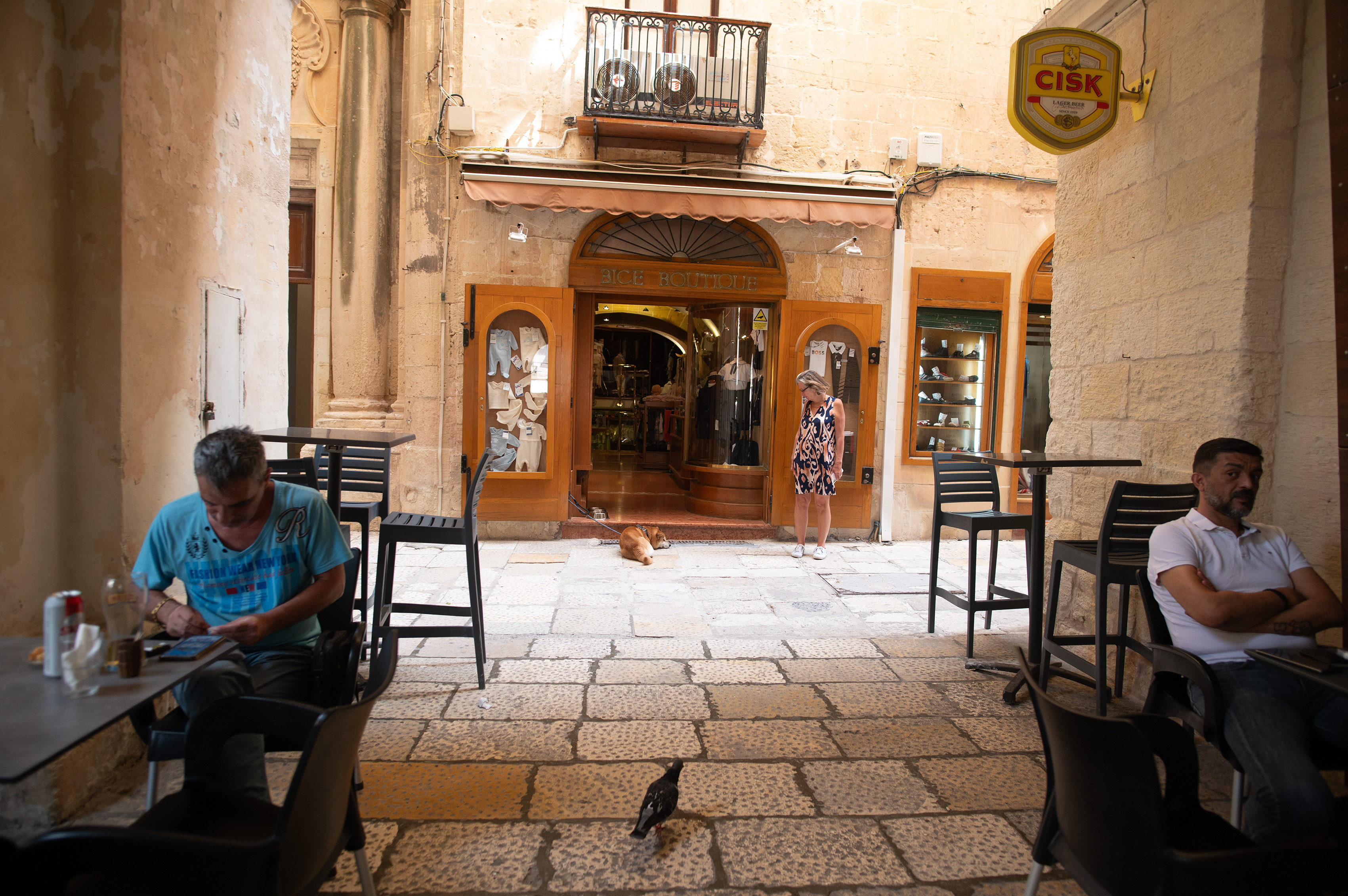 Two men are seated at tables, one engrossed in his phone