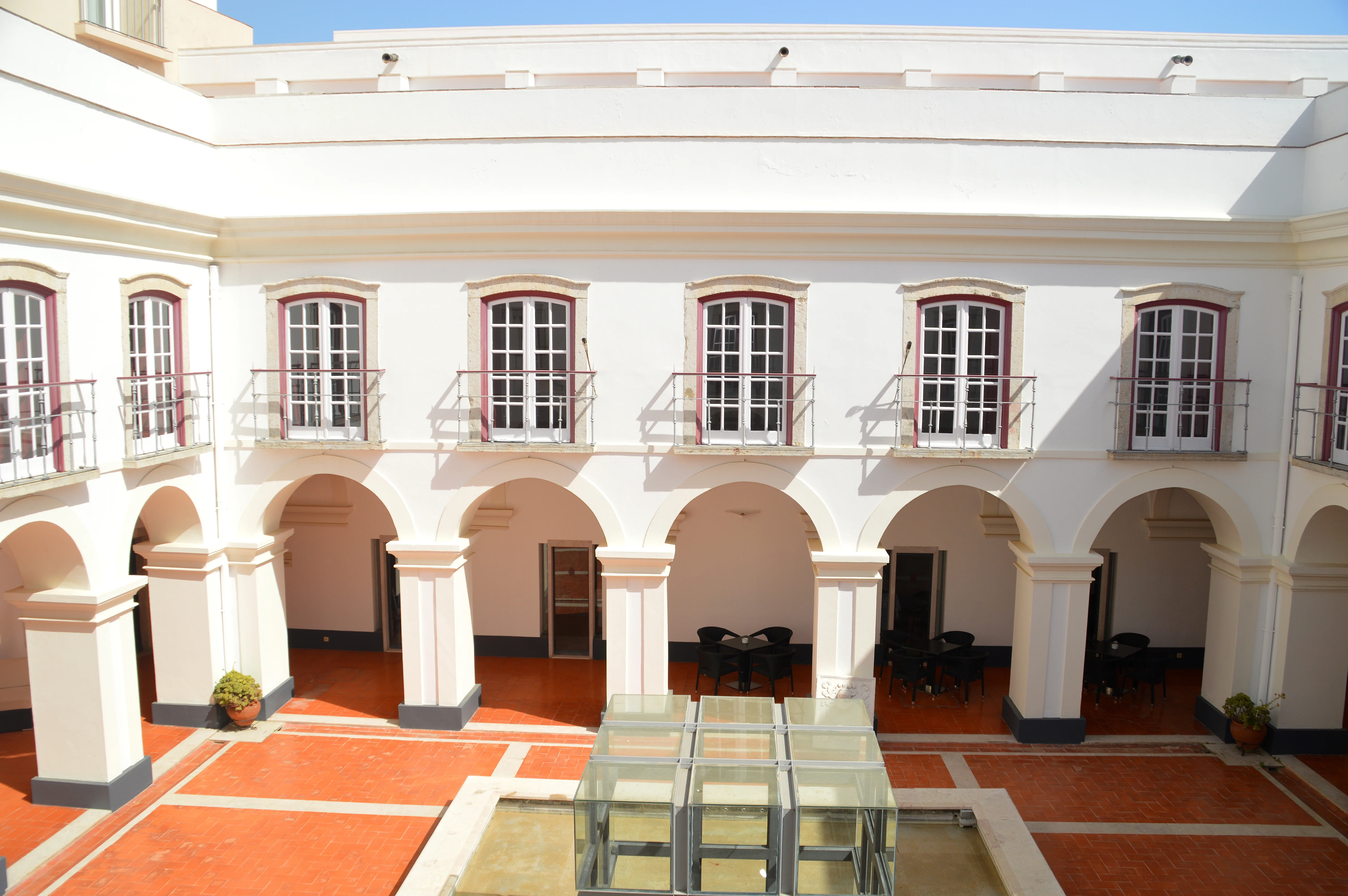 An outdoor courtyard in a building, showing a covered walkway with arches, balconies above, and a paved floor.