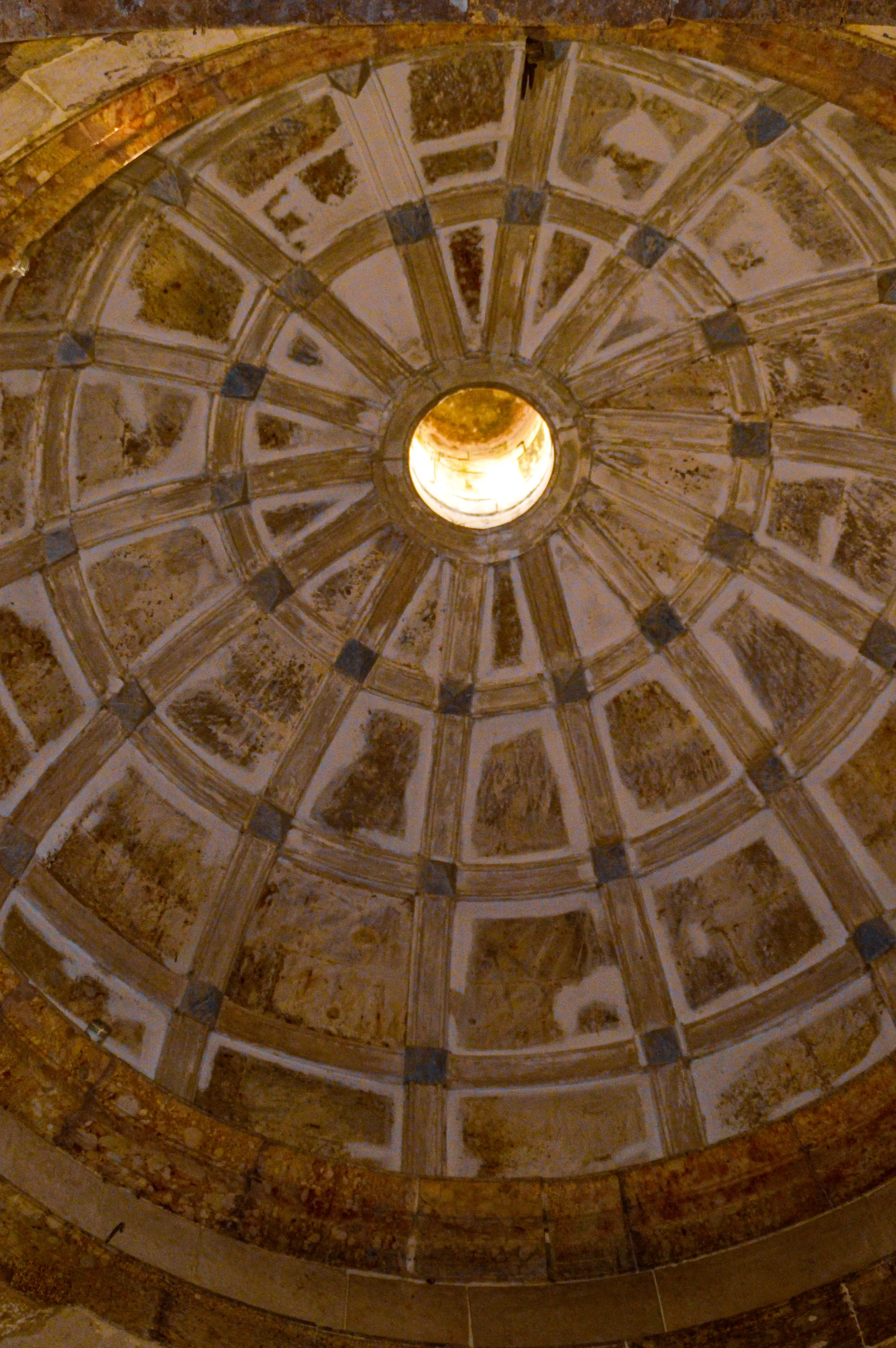 Interior view of an ancient domed ceiling with a circular opening (oculus) at the centre, showing segmented panels and weathered stone textures.