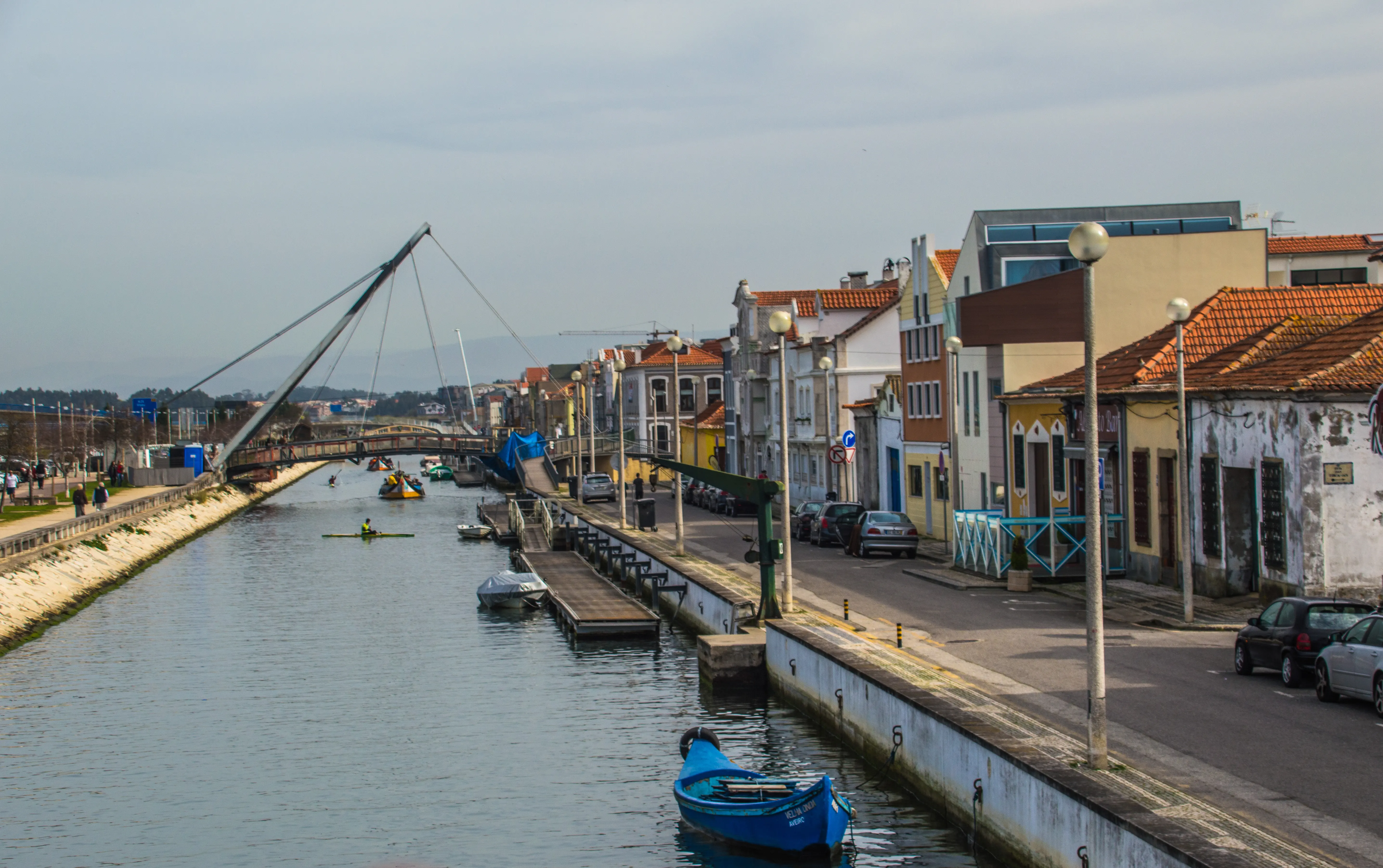 A canal in a European town with colourful buildings, a modern bridge, and people kayaking on the water.