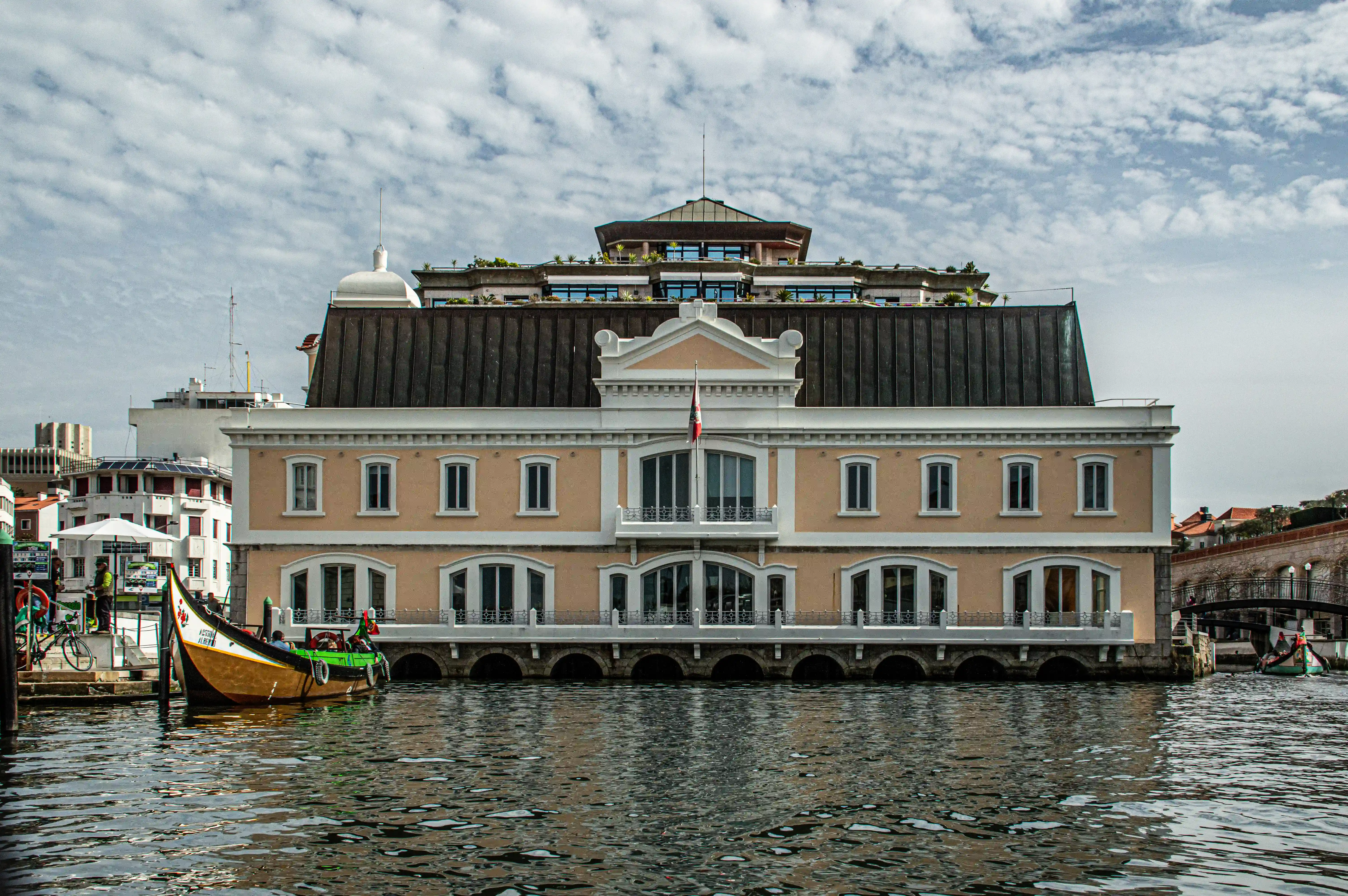 A yellow building with a dark roof is reflected in the water, with a colourful, traditional boat in the foreground.