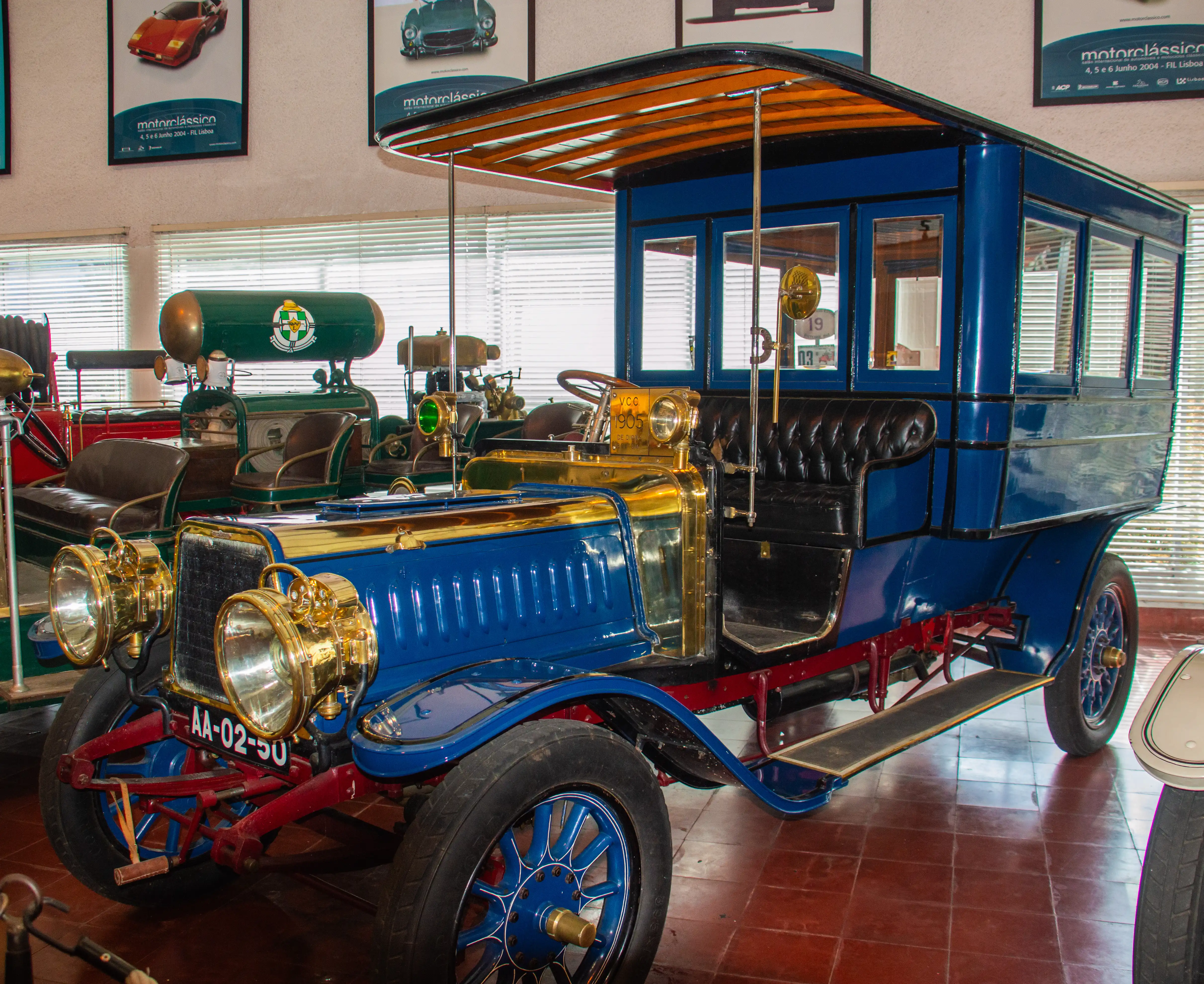 A vintage blue omnibus with brass accents and a wooden roof stands on a tiled floor, with posters in the background.