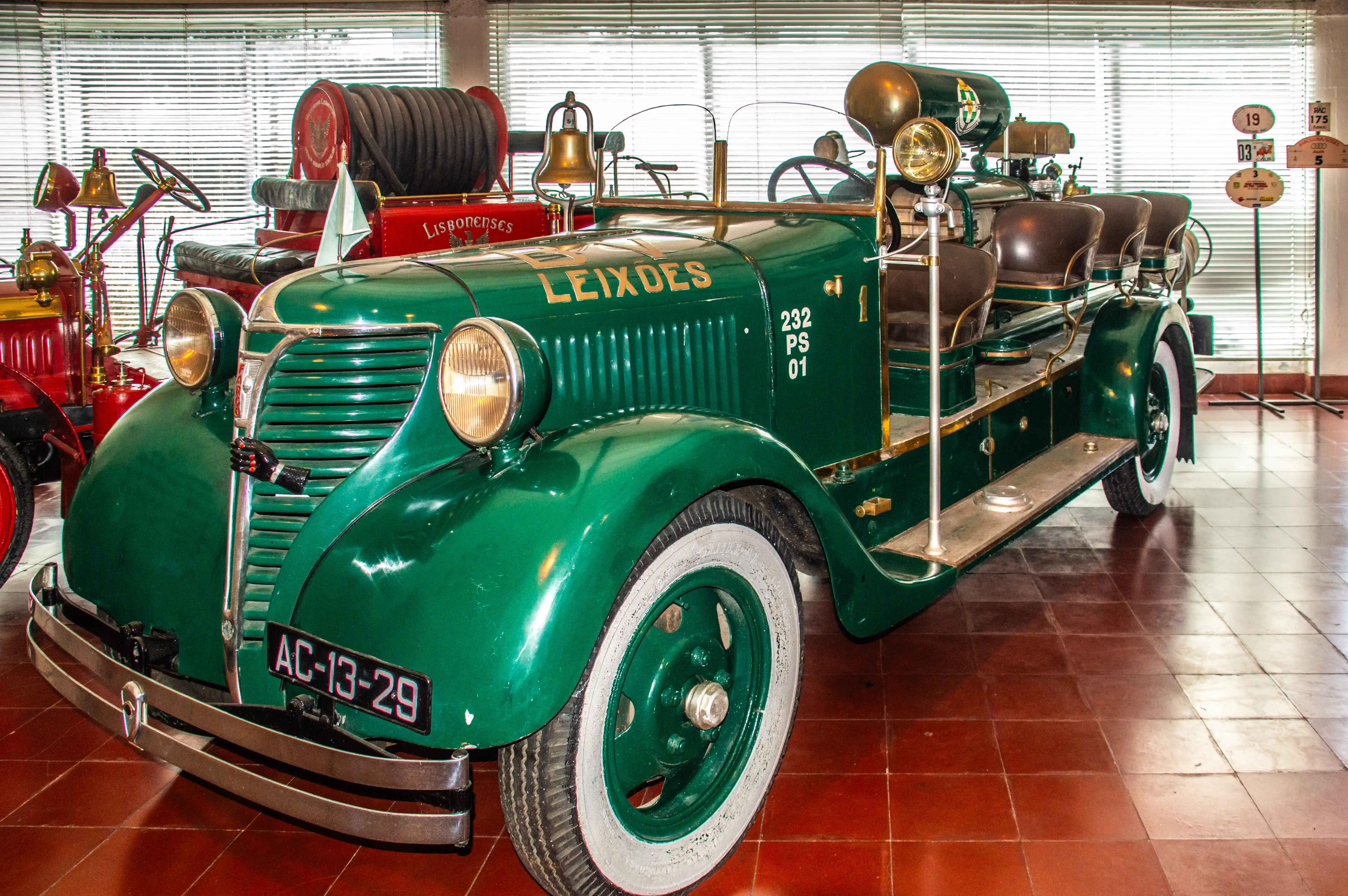 A vintage green fire engine with gold lettering LEIXDES and a brass bell is parked indoors