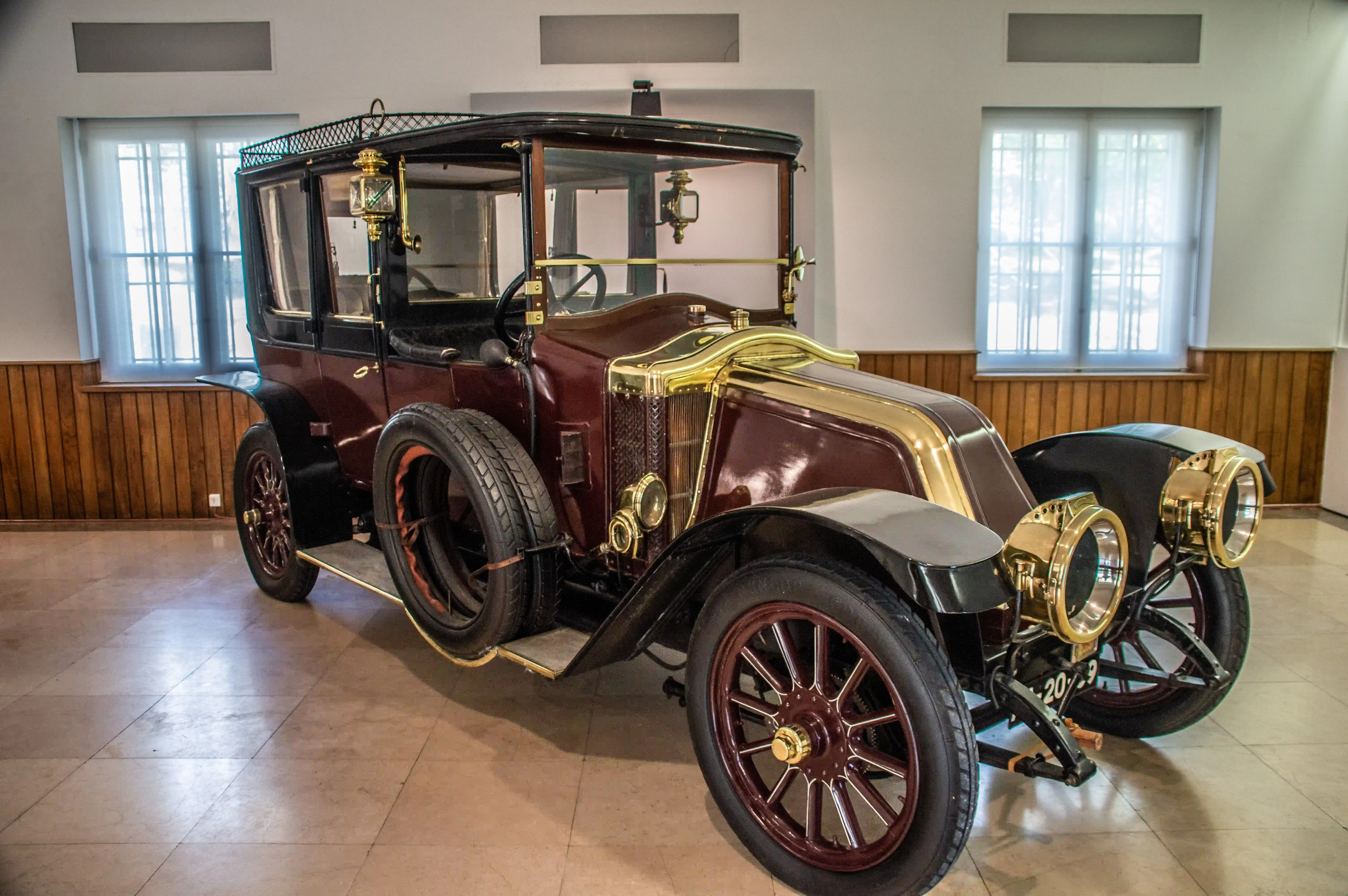 A maroon and gold vintage Renault landaulet car with spoked wheels and two large brass headlamps, displayed indoors.