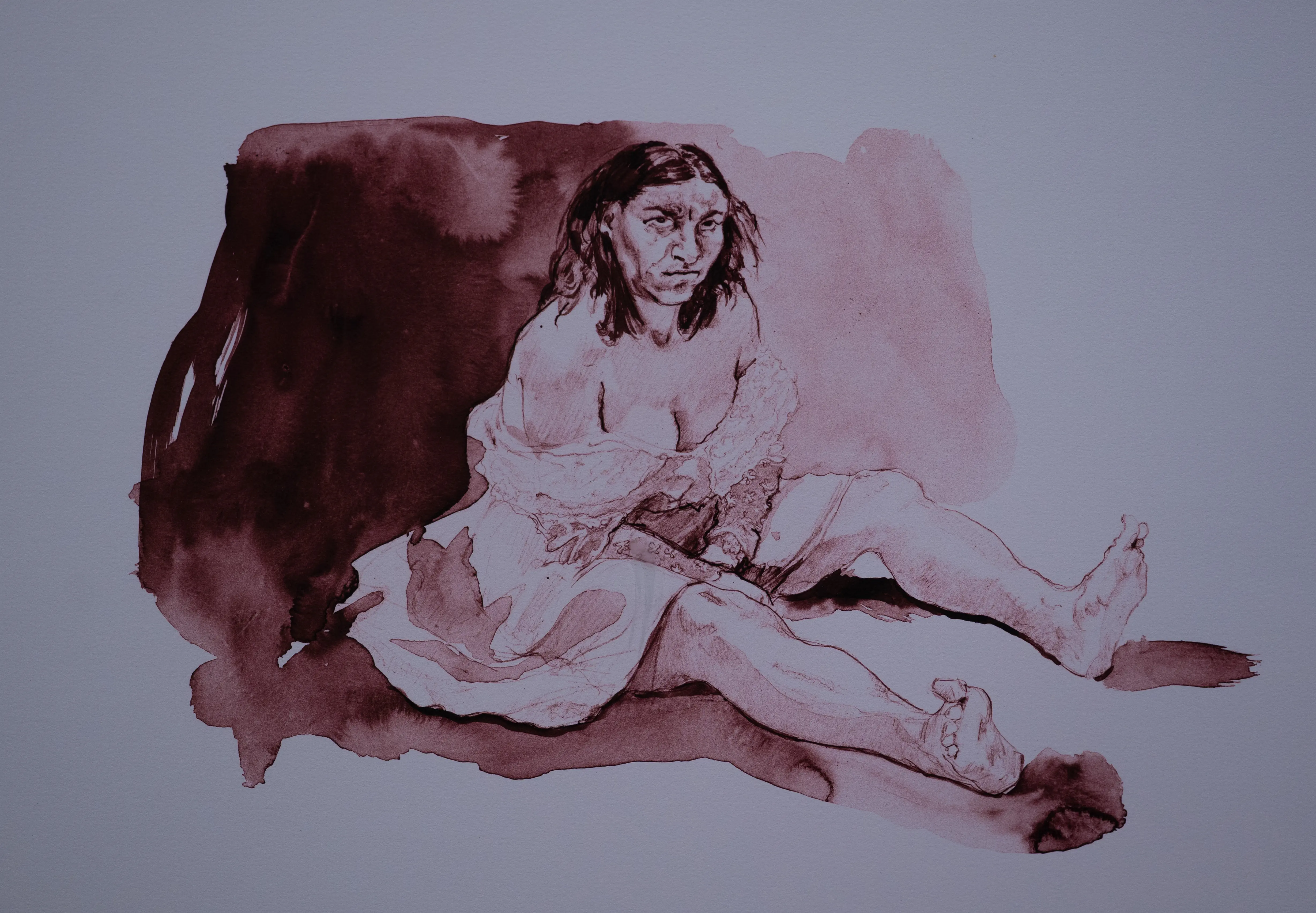Ink wash drawing of a woman with dark hair and an intense expression, seated with her legs extended. She wears a loose white garment.