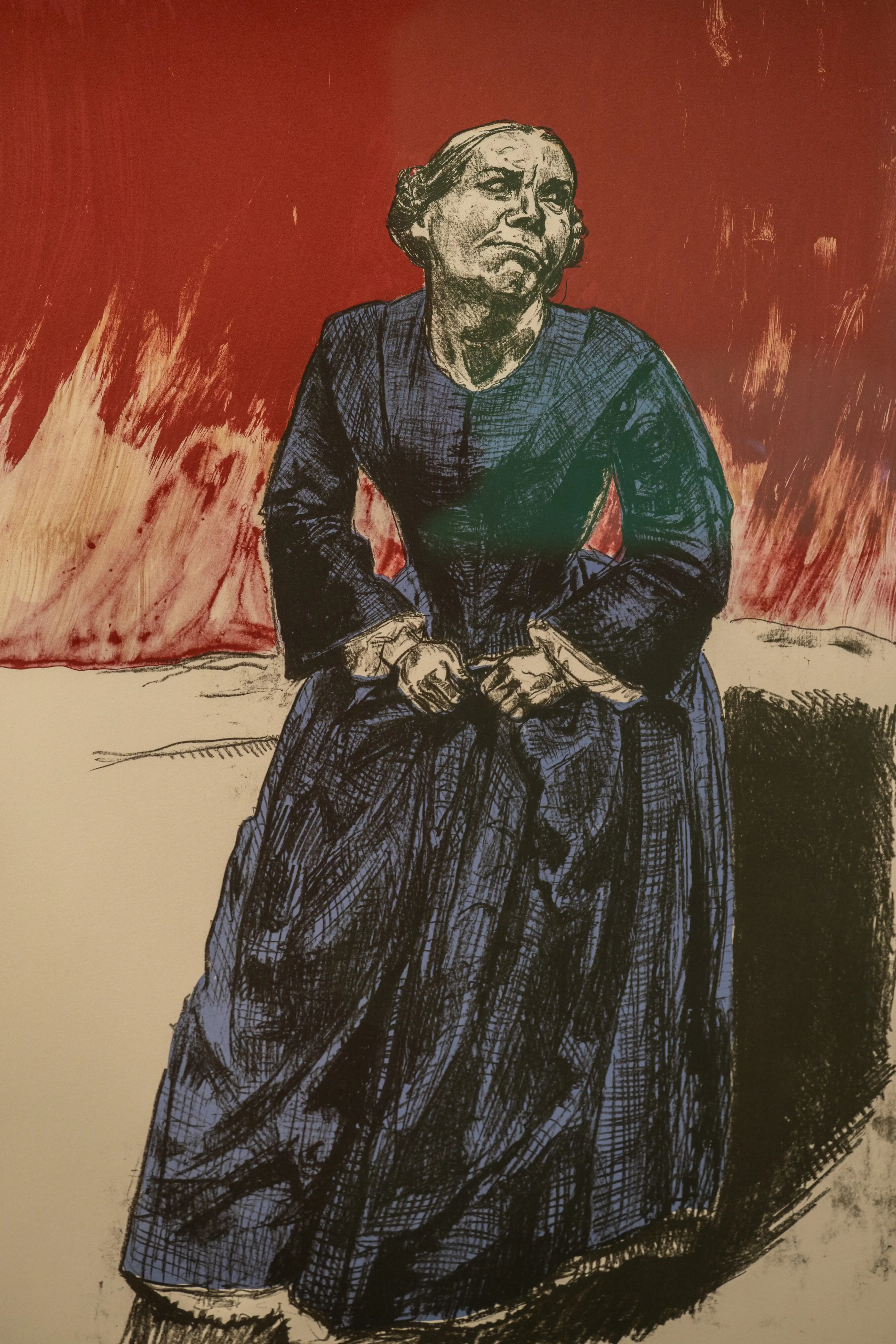 A lithograph or print of a woman with an intense facial expression, wearing a dark blue dress, standing against a red and white background that resembles flames.