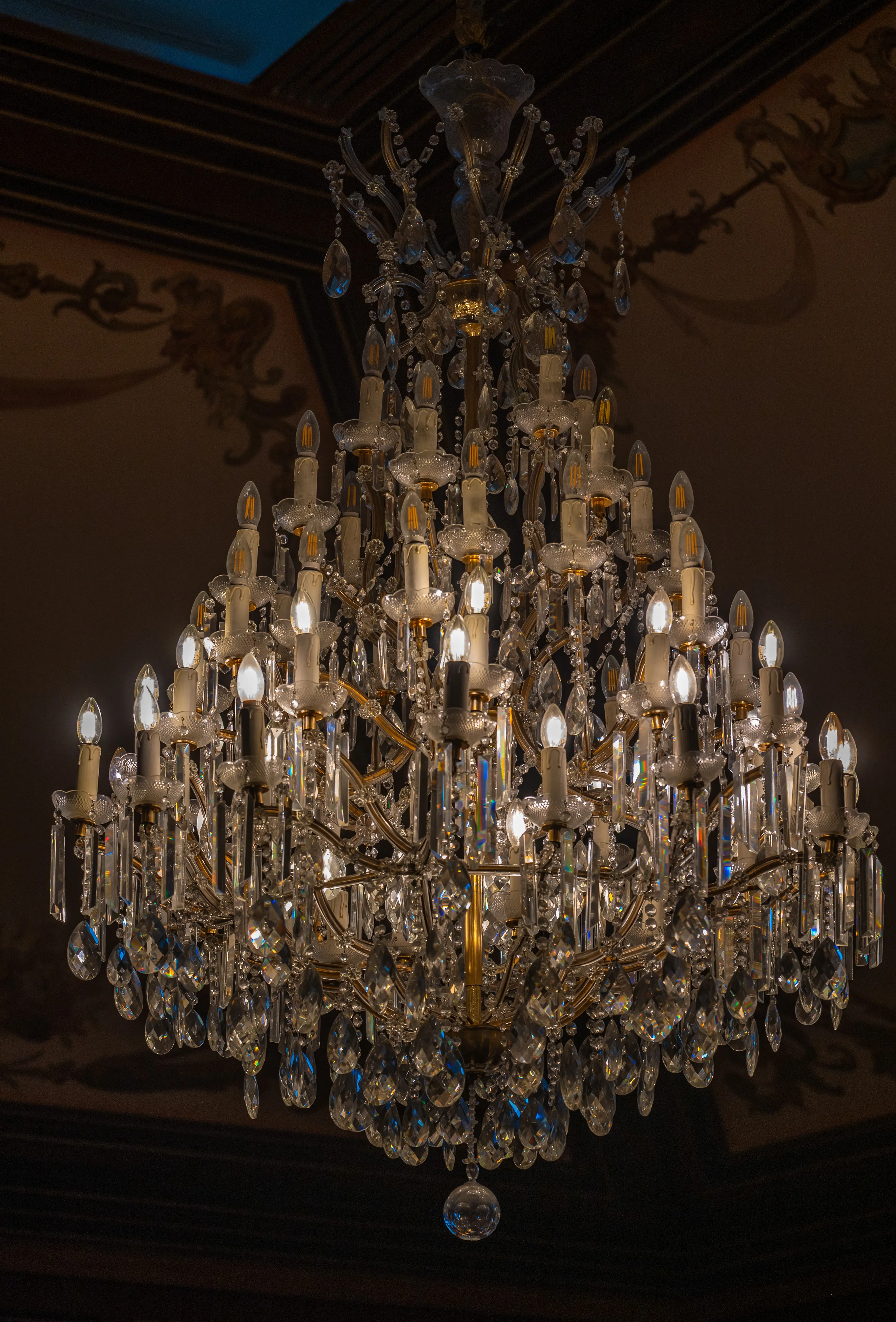  A detailed shot of a large, elaborate crystal chandelier with many lights and hanging prisms, set against a dark background.