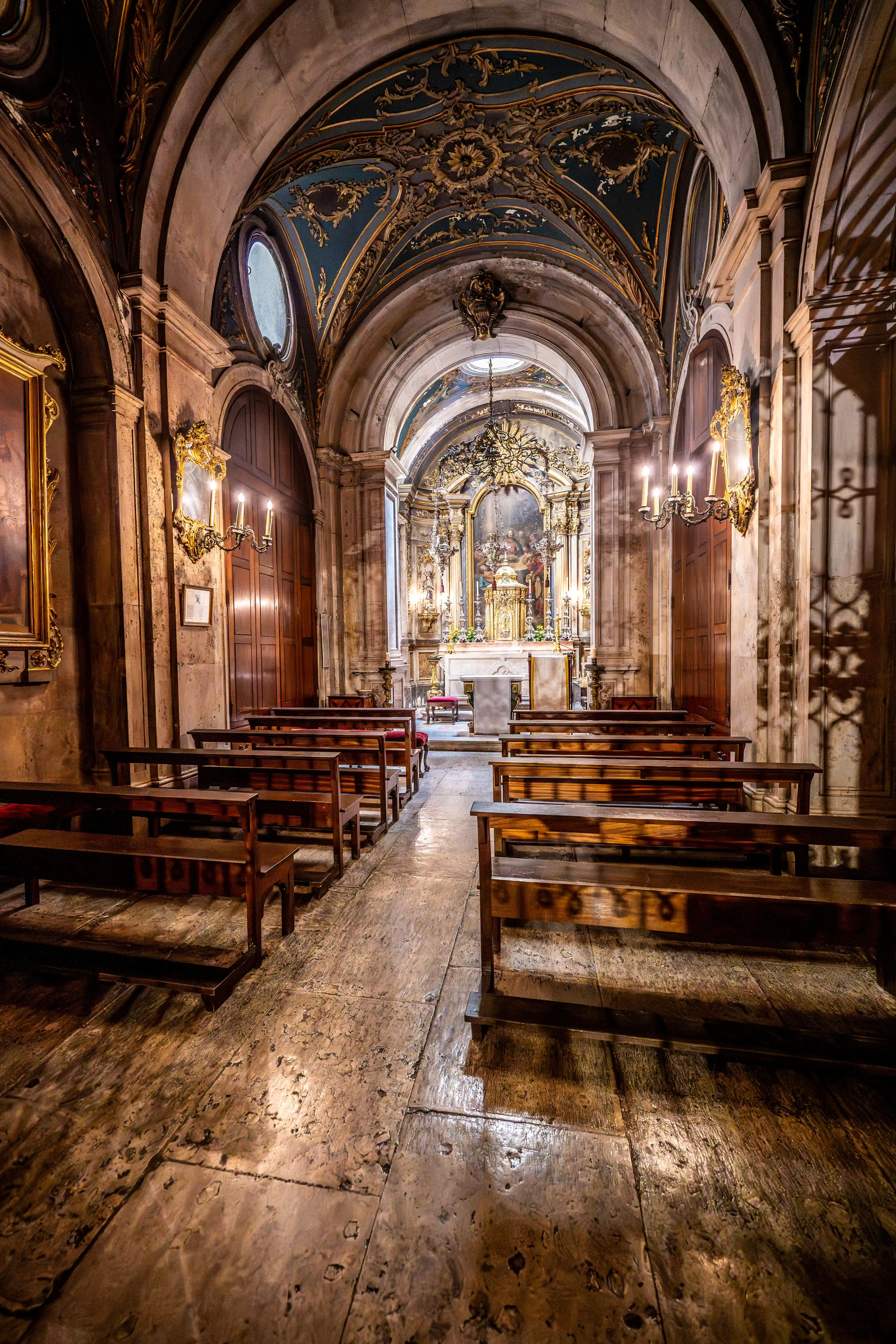 Interior view of a church with rows of wooden pews facing a brightly lit, ornate altar and gilded ceiling decorations.