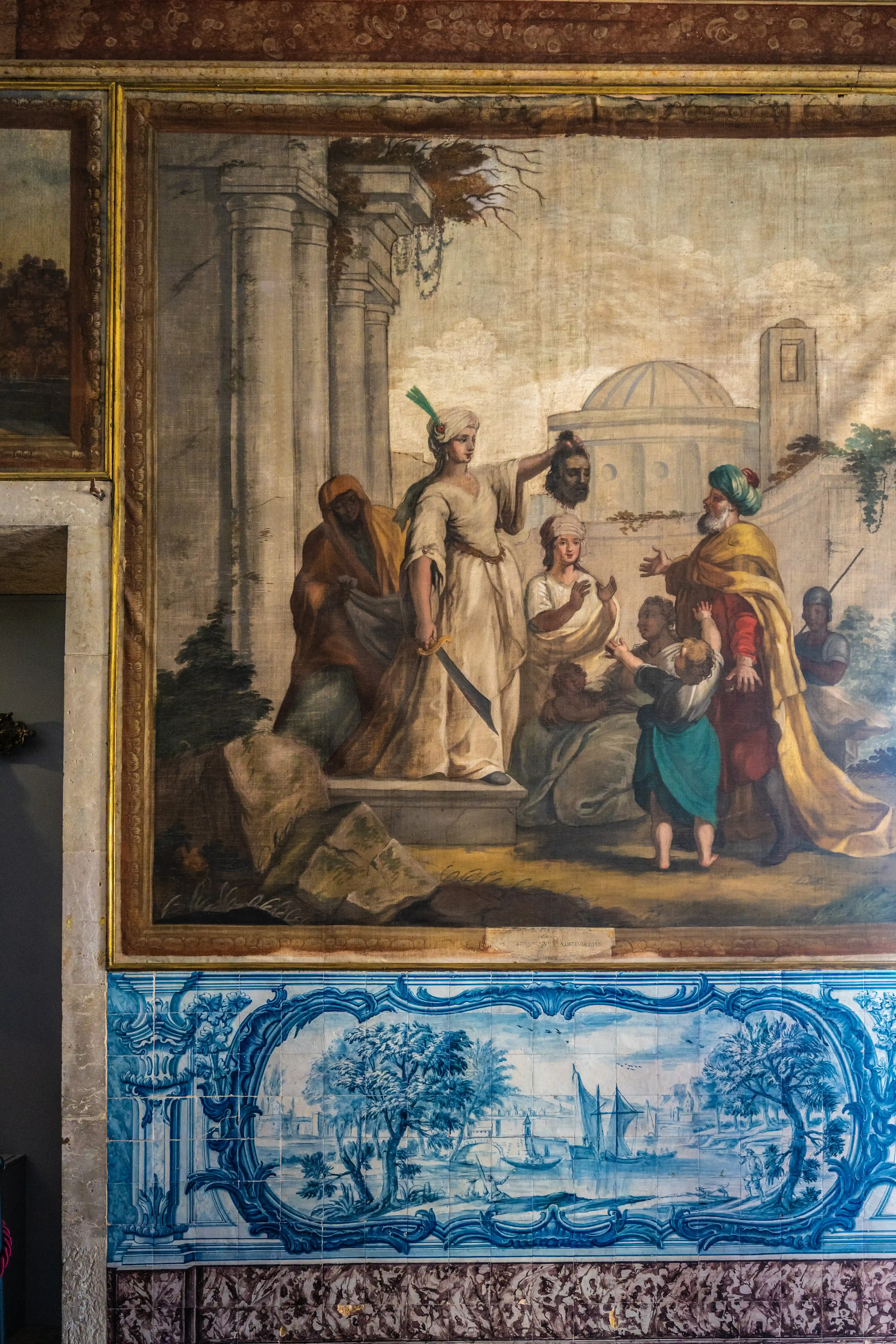 A grand fresco painting showing a scene with a woman holding a severed head, and other figures. Below the fresco is a detailed blue and white tiled panel with a pastoral landscape.