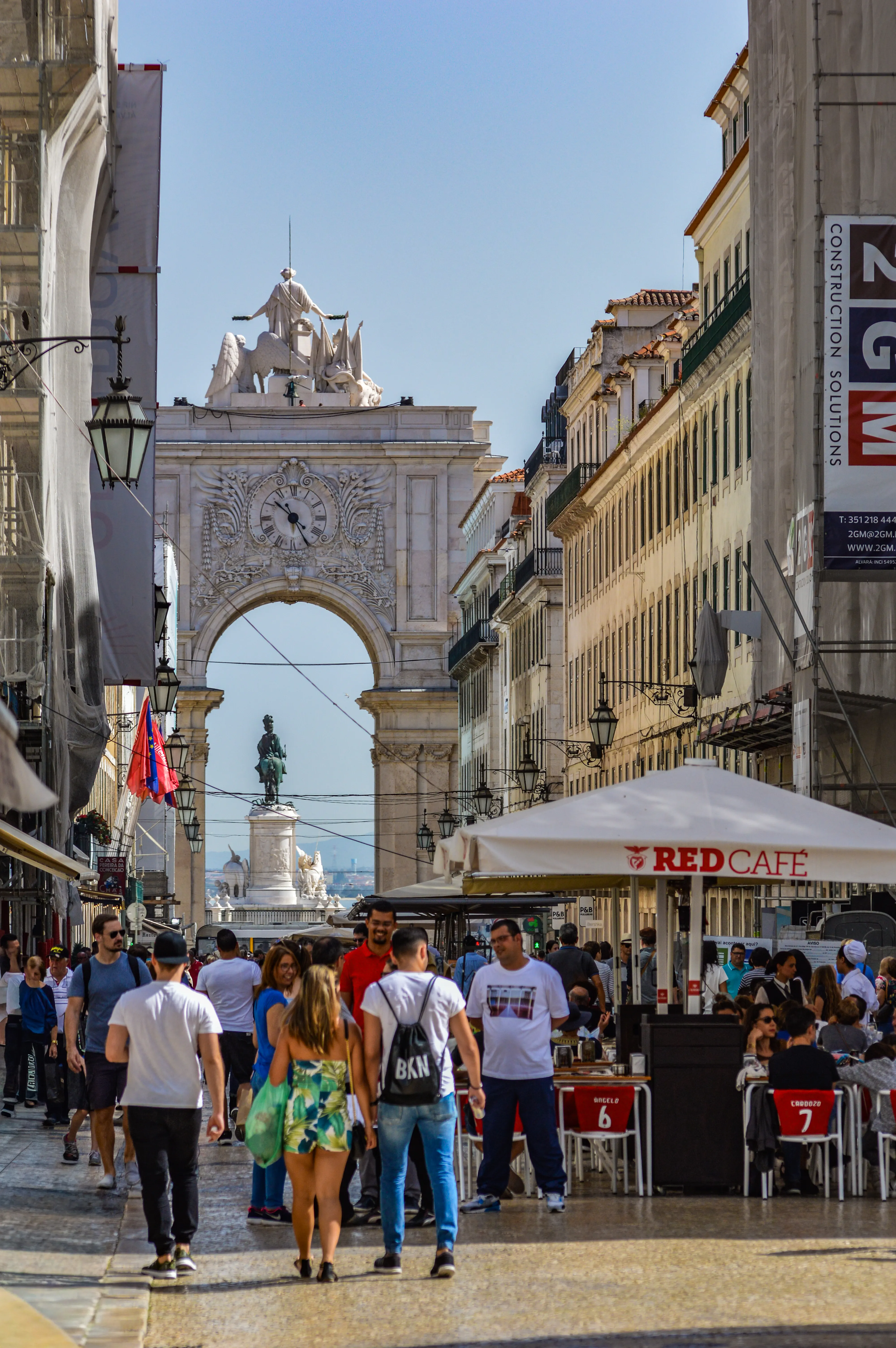A view through the Rua Augusta Arch in Lisbon, with a street full of people and outdoor cafe seating on the right.