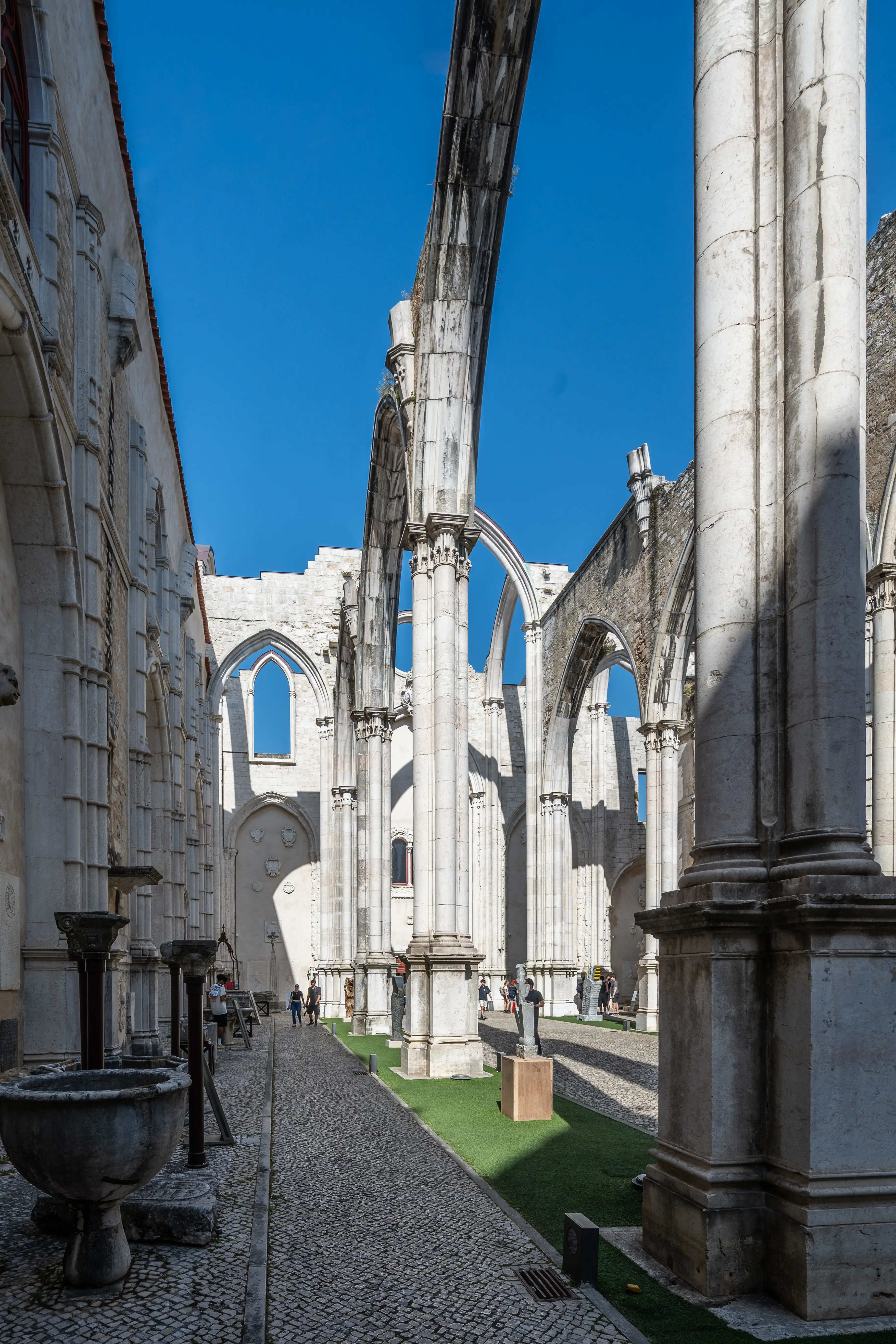  Sunlight streaming through the arches of ancient stone ruins, illuminating a cobbled path and scattered visitors.