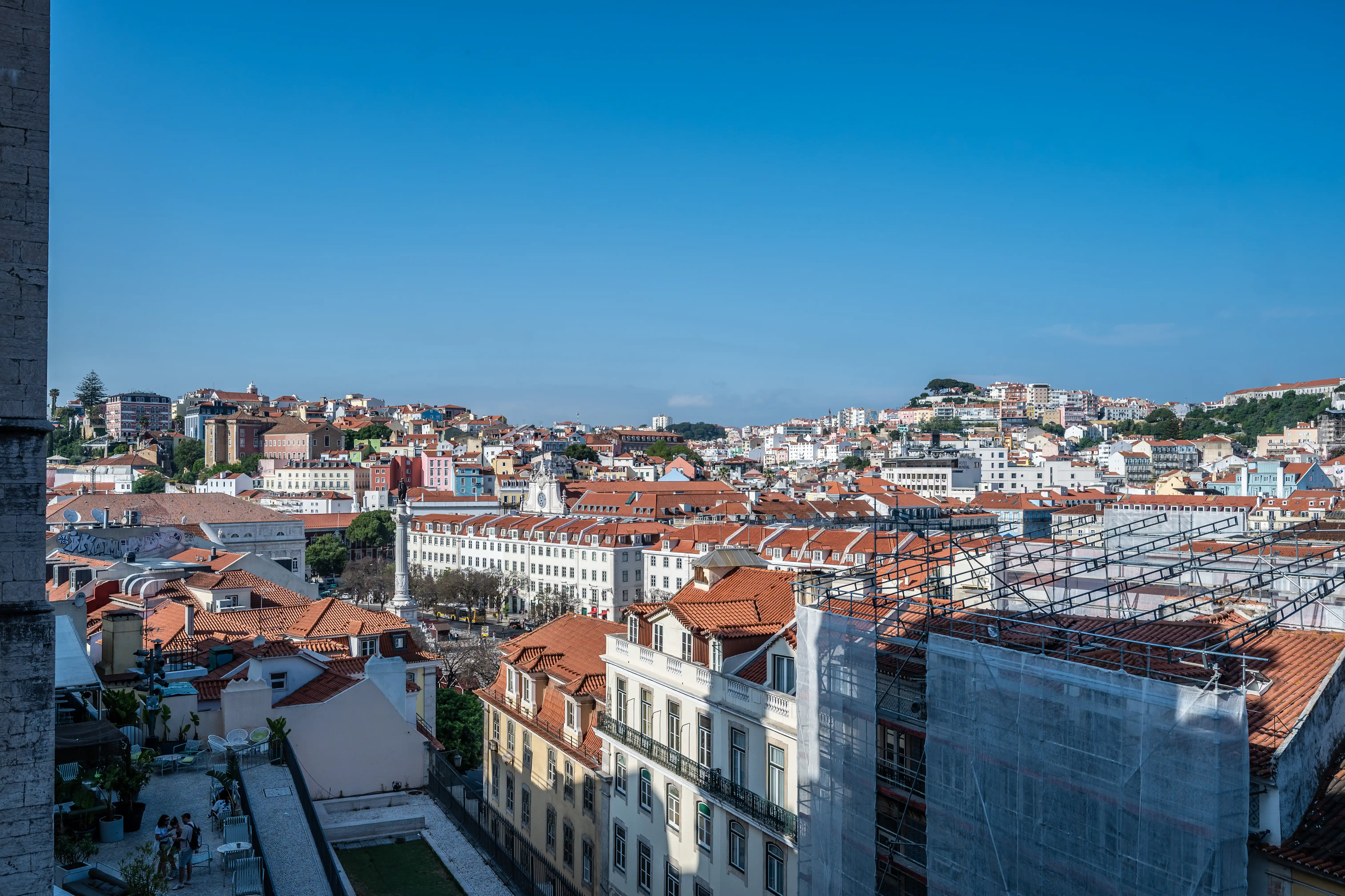 A wide shot of Lisbon's cityscape featuring numerous buildings with red-tiled roofs under a clear blue sky.