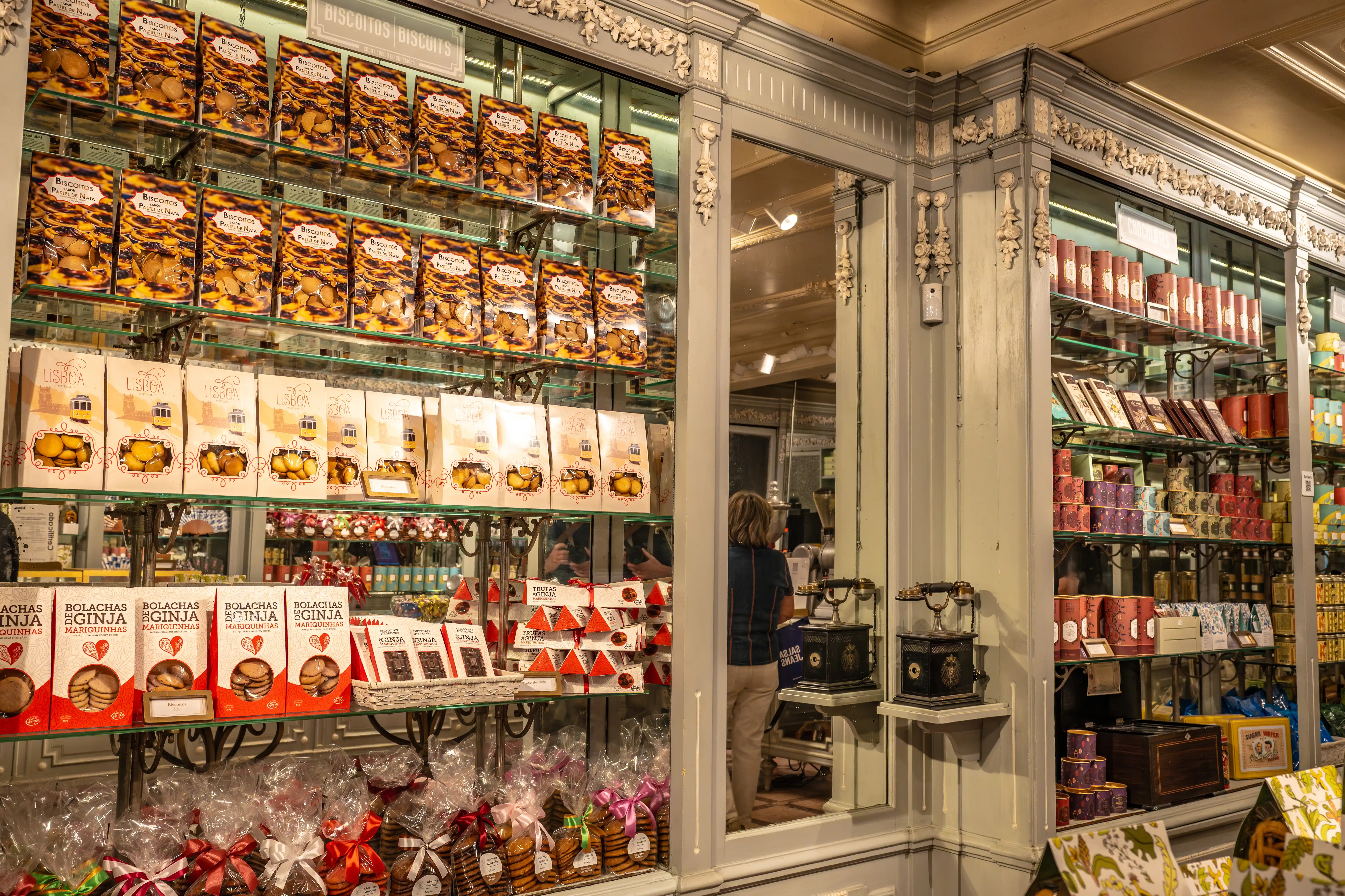 Shelves filled with various boxes and packets of Portuguese biscuits and chocolates in a traditional shop. Some packaging displays images of Lisbon trams.