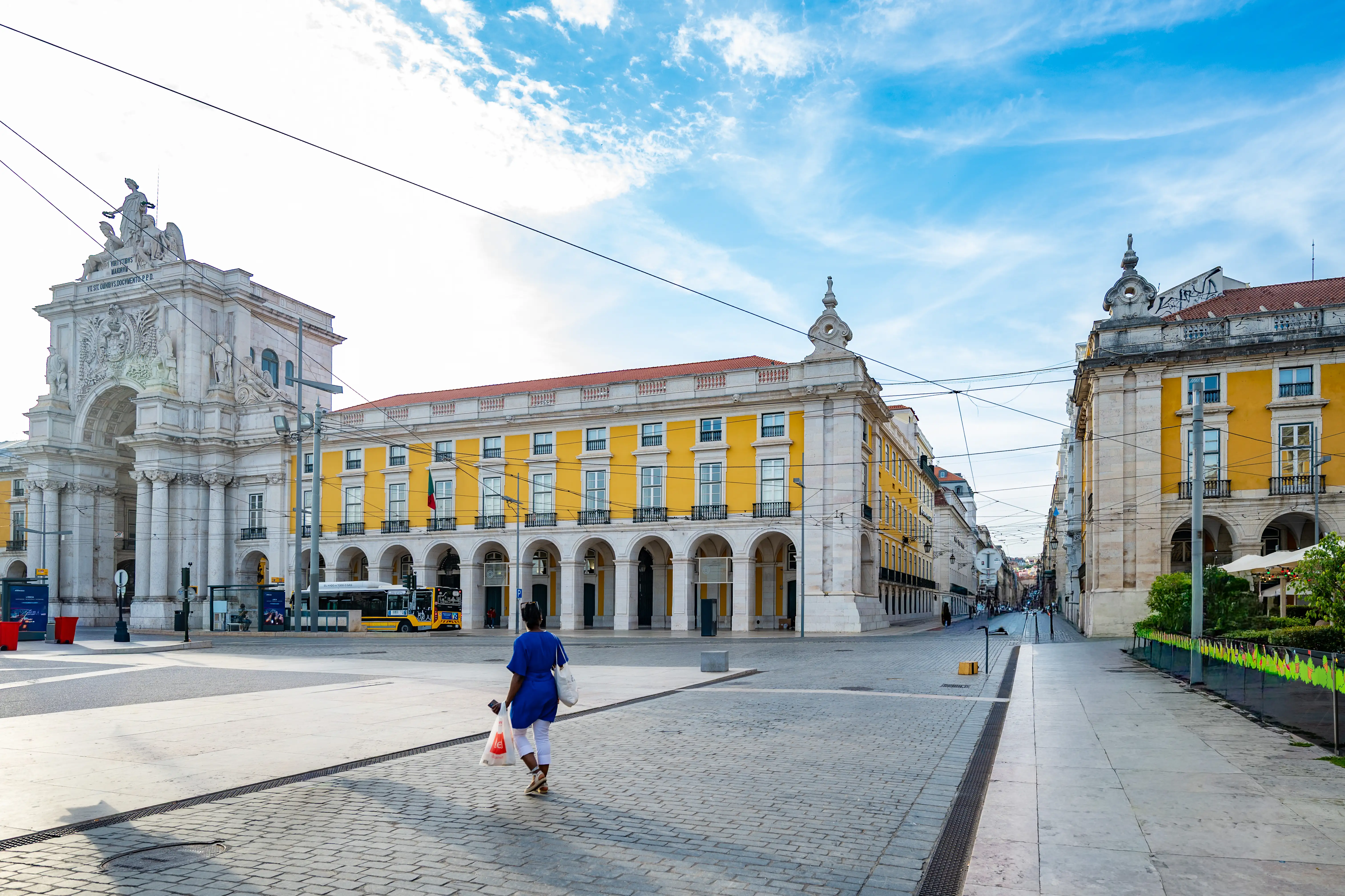 People walking in a European square with ornate buildings and an archway.