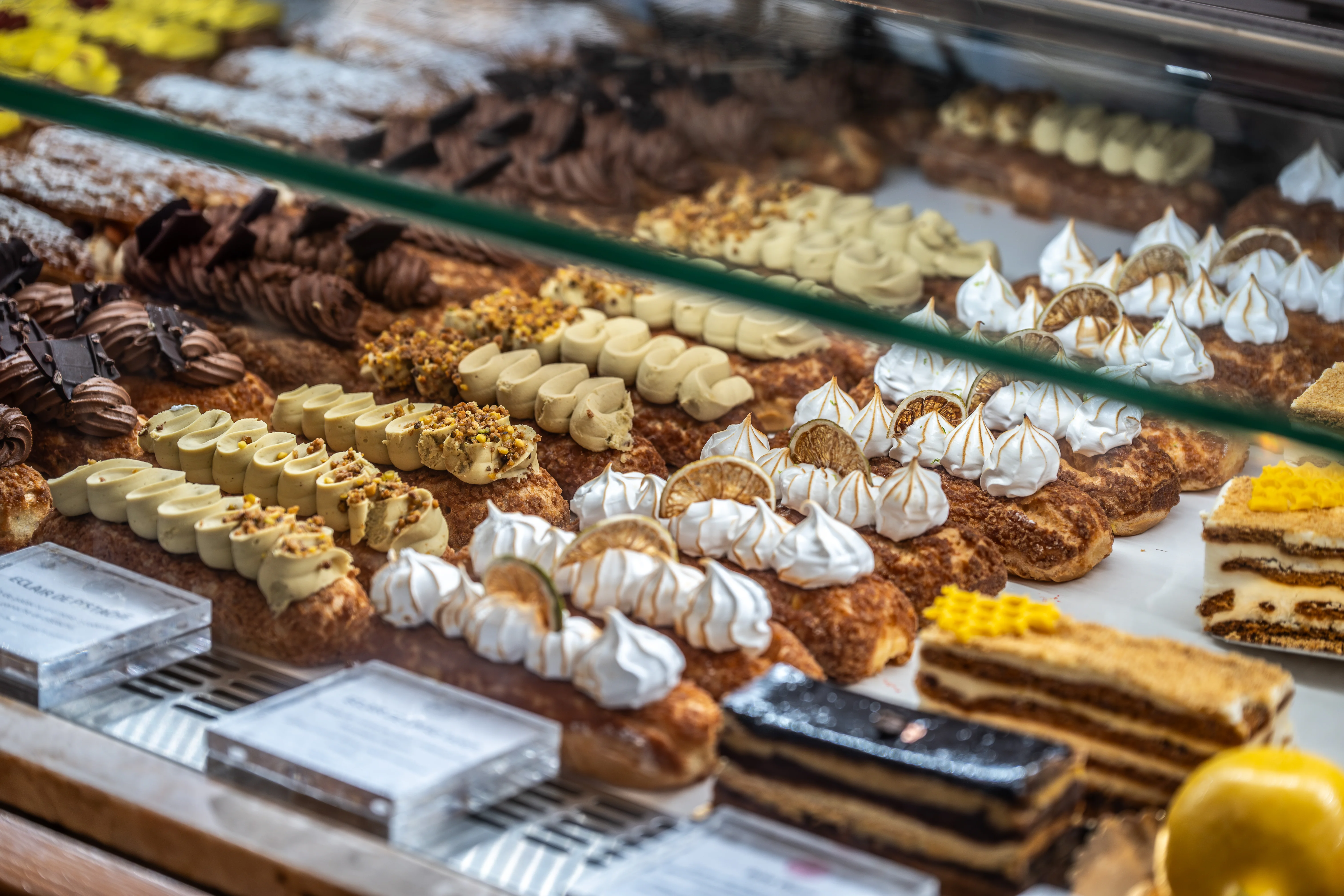 A close-up of a pastry display case showcasing an assortment of artisanal eclairs and cakes with various toppings.