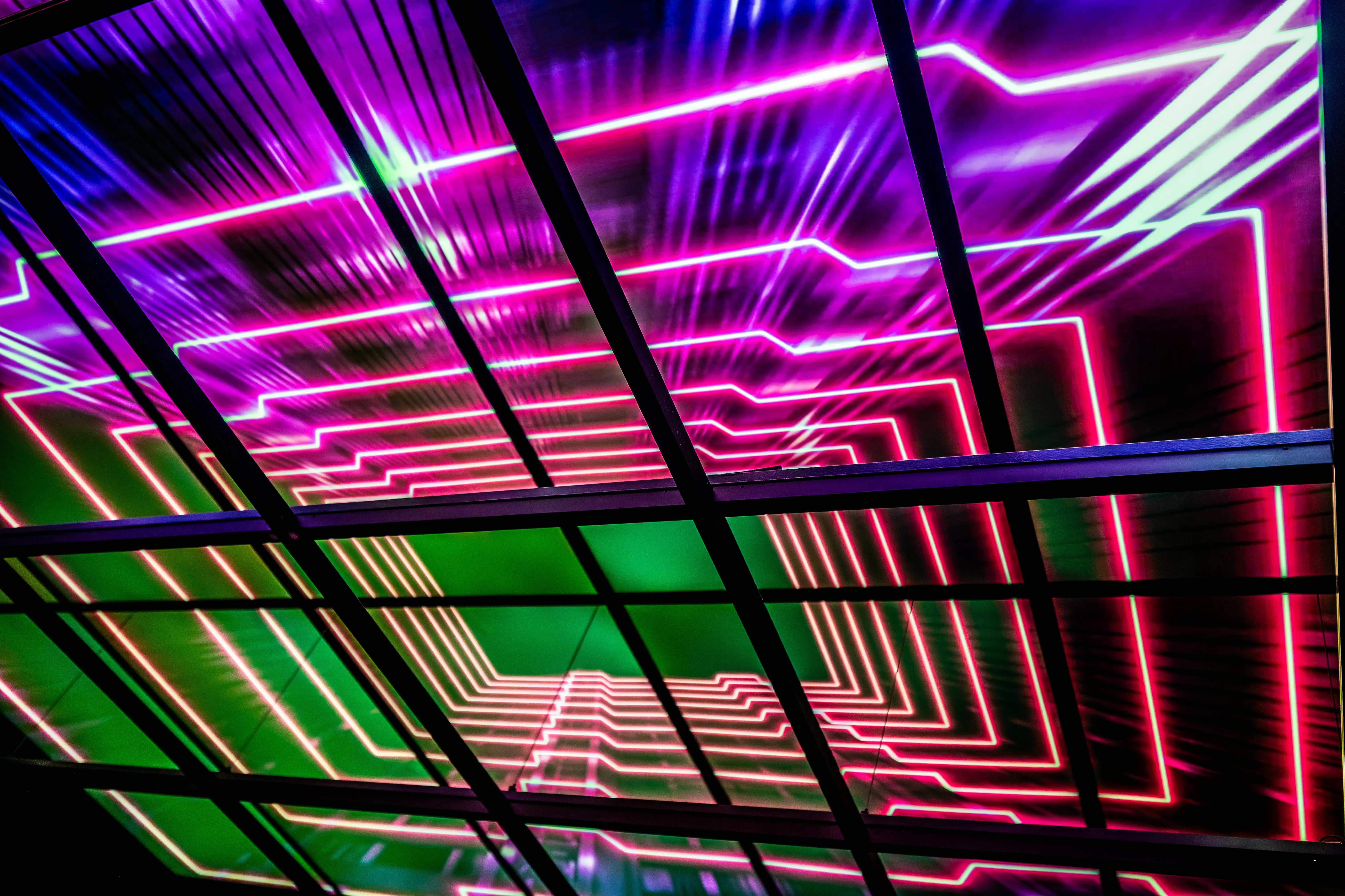  A dark ceiling with angular frames overlaid on a vibrant neon light display of pink and purple geometric lines receding into the distance.