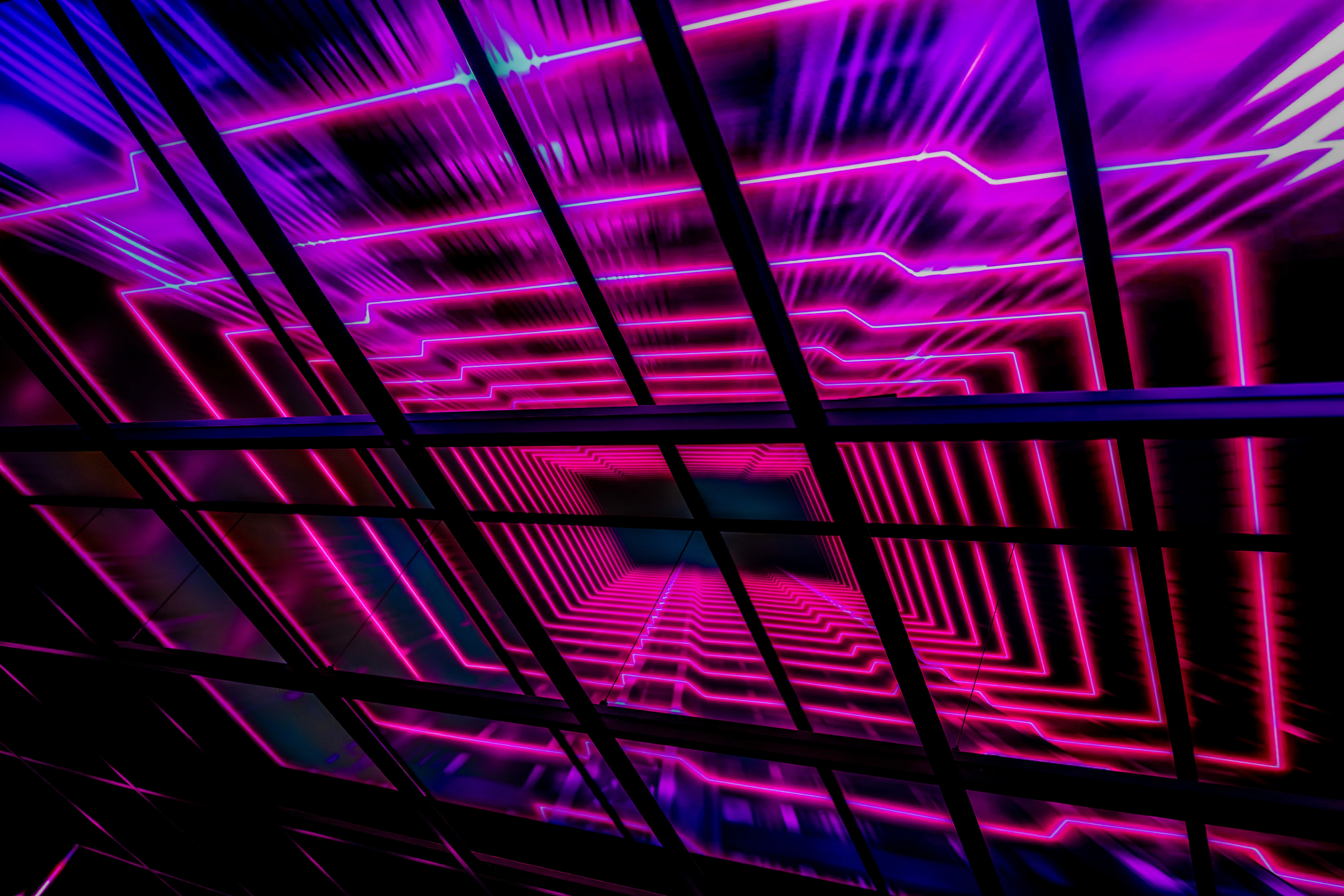  A dark ceiling with angular frames overlaid on a vibrant neon light display of pink and purple geometric lines receding into the distance.