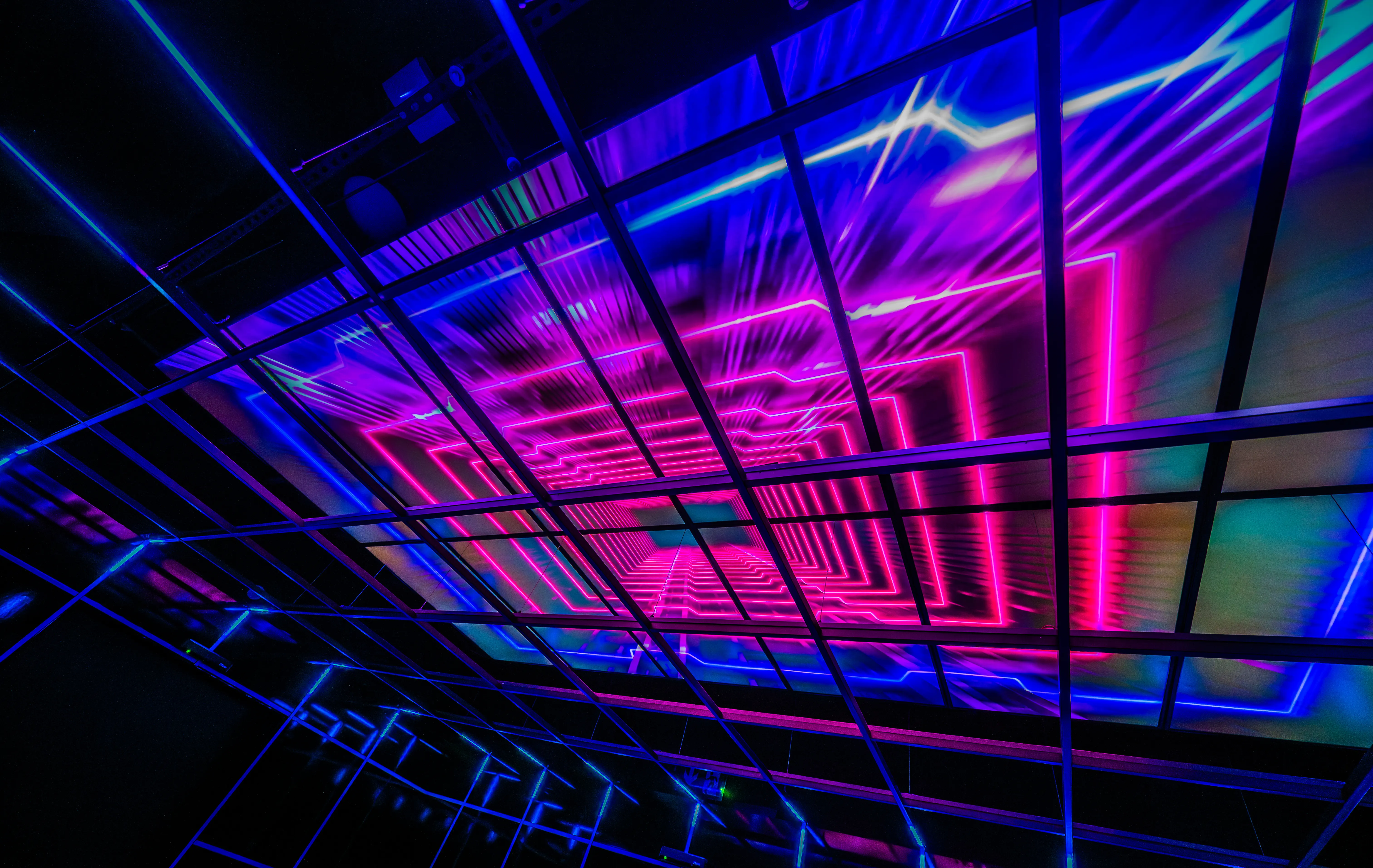 Abstract image of a perspective tunnel made of glowing pink and blue neon squares, framed by a dark metal grid.