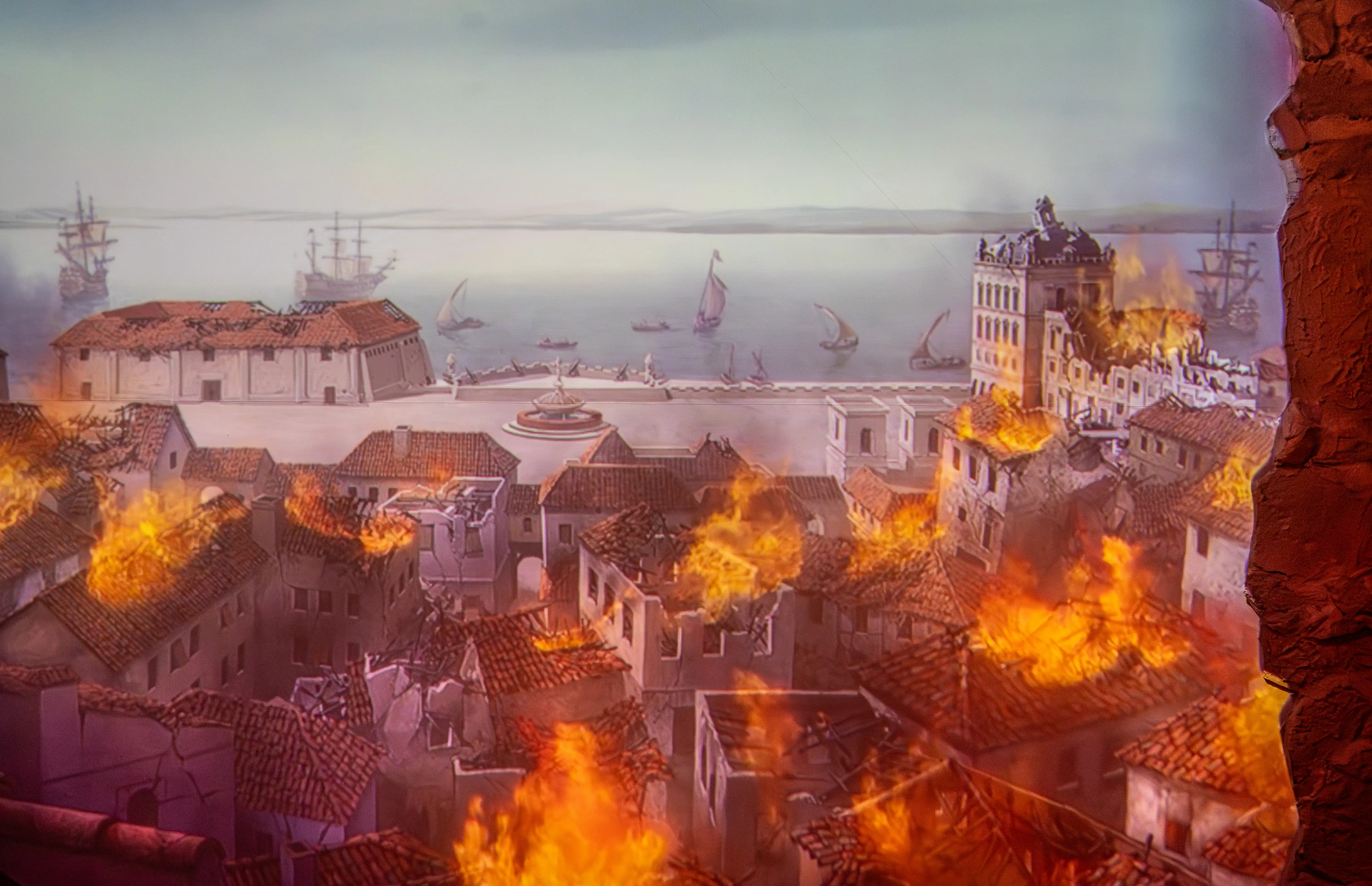 An illustration of a burning coastal town with ships in the harbour, viewed through a rocky opening.