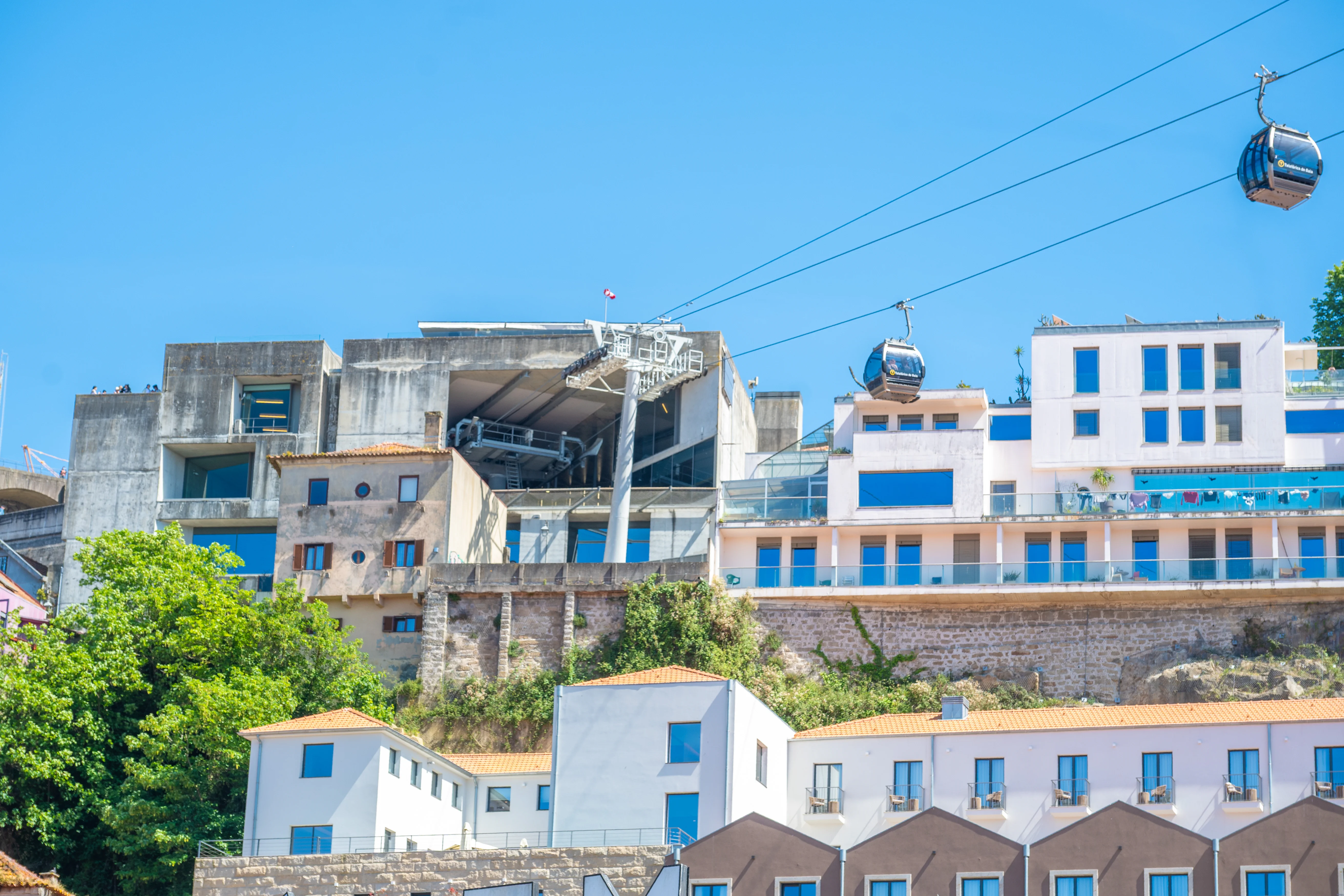 A view of a cable car system traversing a hillside city with various architectural styles of buildings under a clear blue sky.