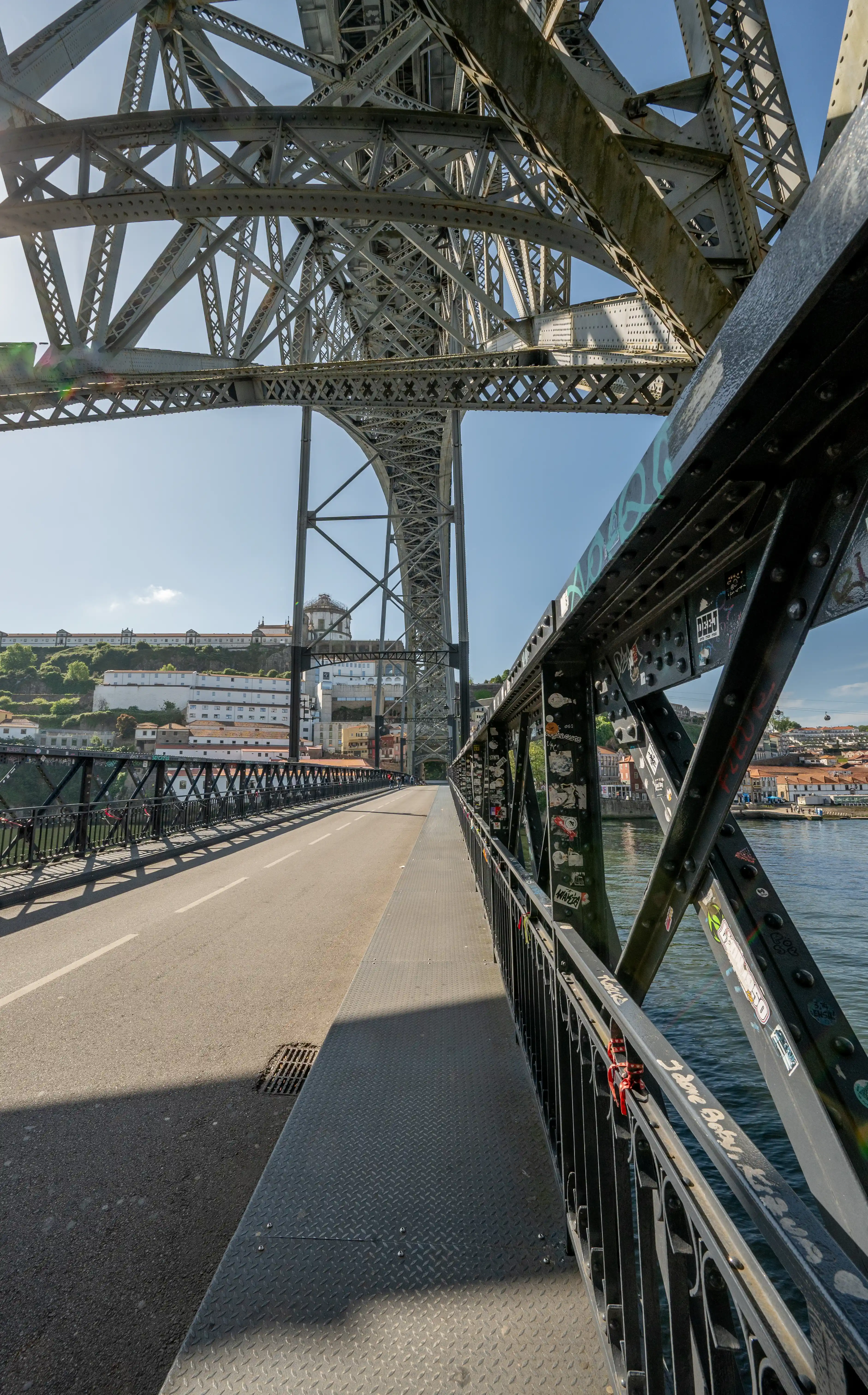 View from the walkway of the Dom Luís I Bridge, Porto, showing the intricate metalwork, the road, the Douro River, and the cityscape of Porto.