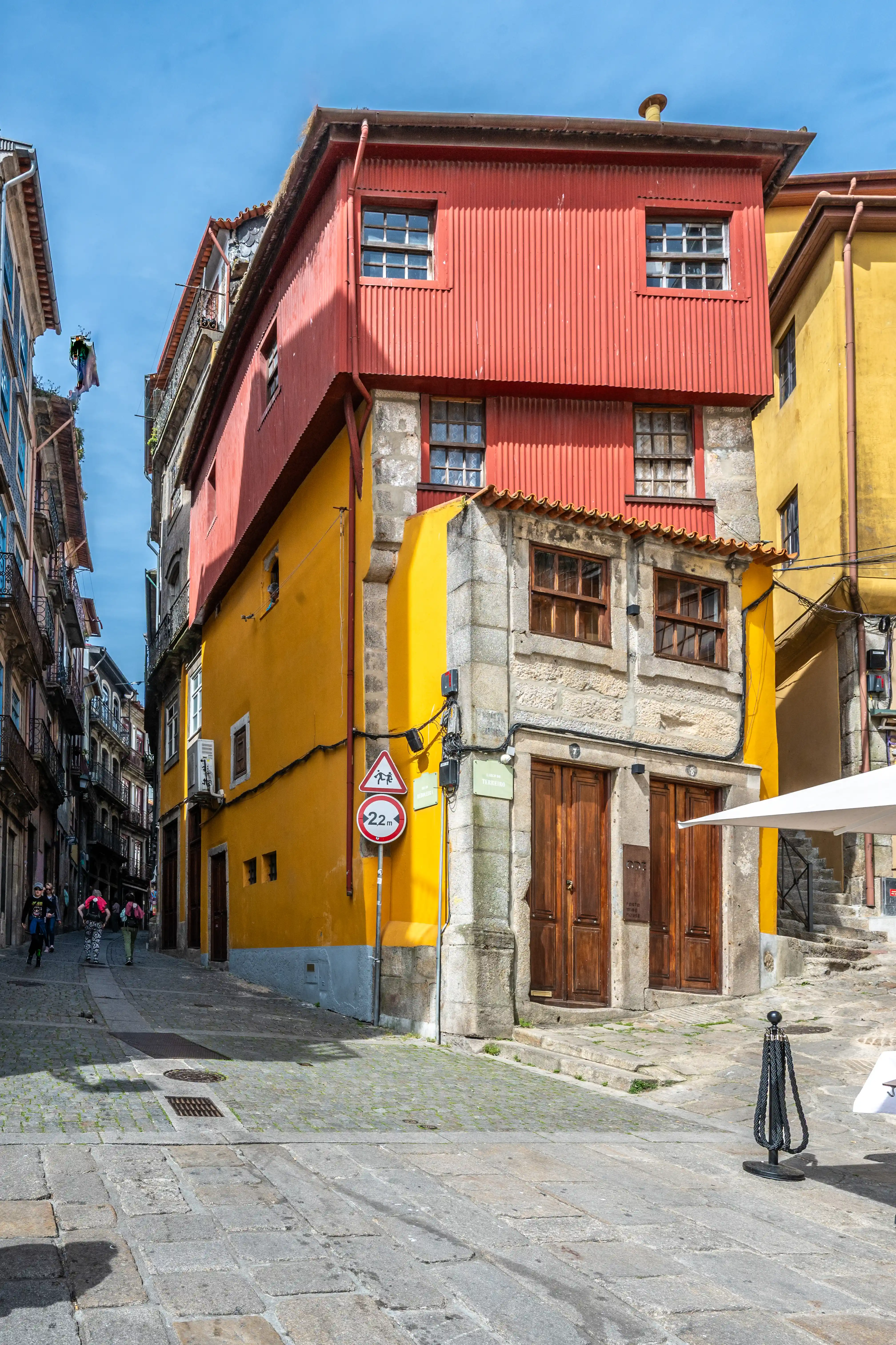 A bright yellow and red building with corrugated metal siding stands on a cobbled street in Porto, Portugal, with traditional wooden doors and windows.