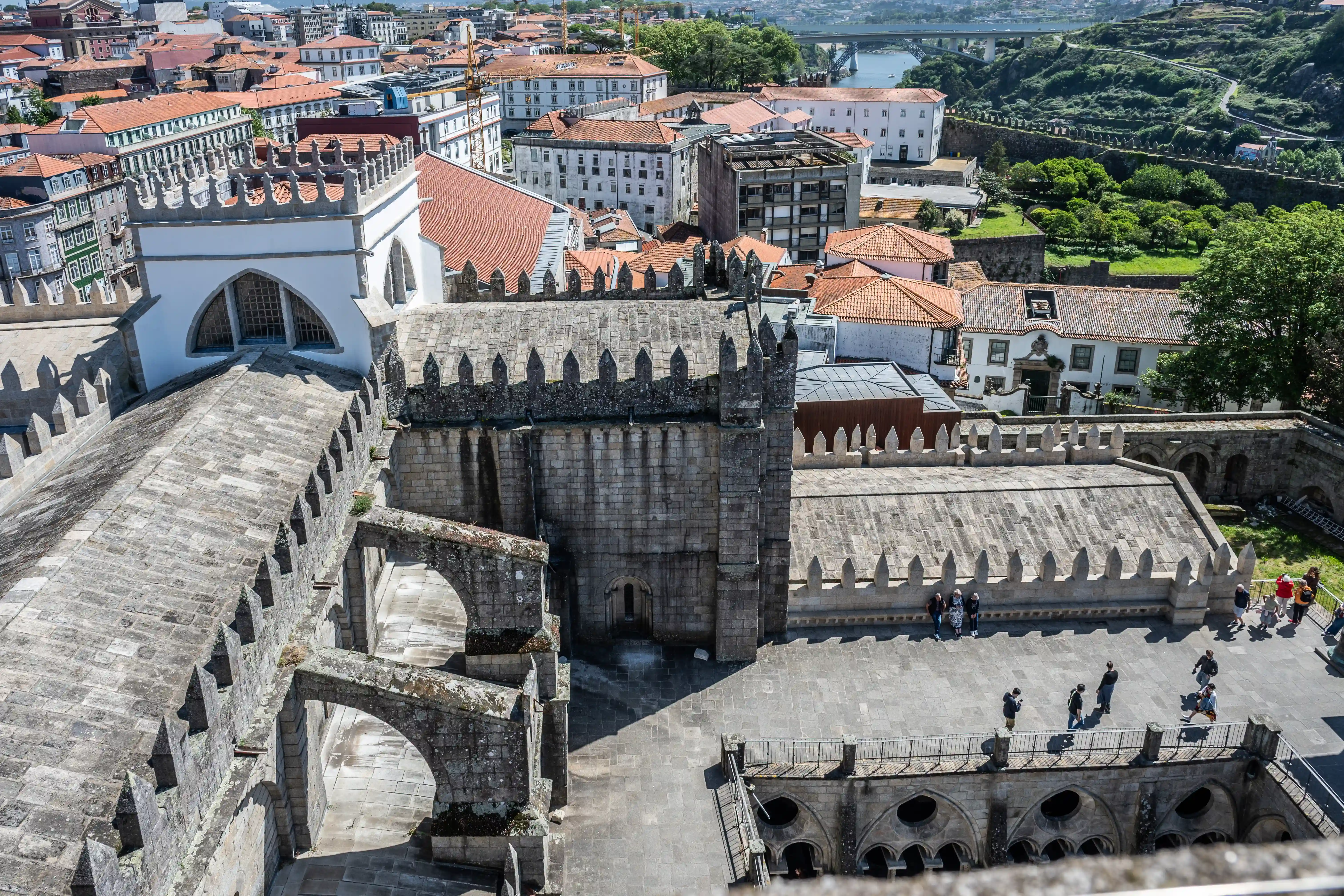 Aerial view of Porto Cathedral with its stone cloisters and battlements overlooking the city's rooftops, a river, and a distant bridge.