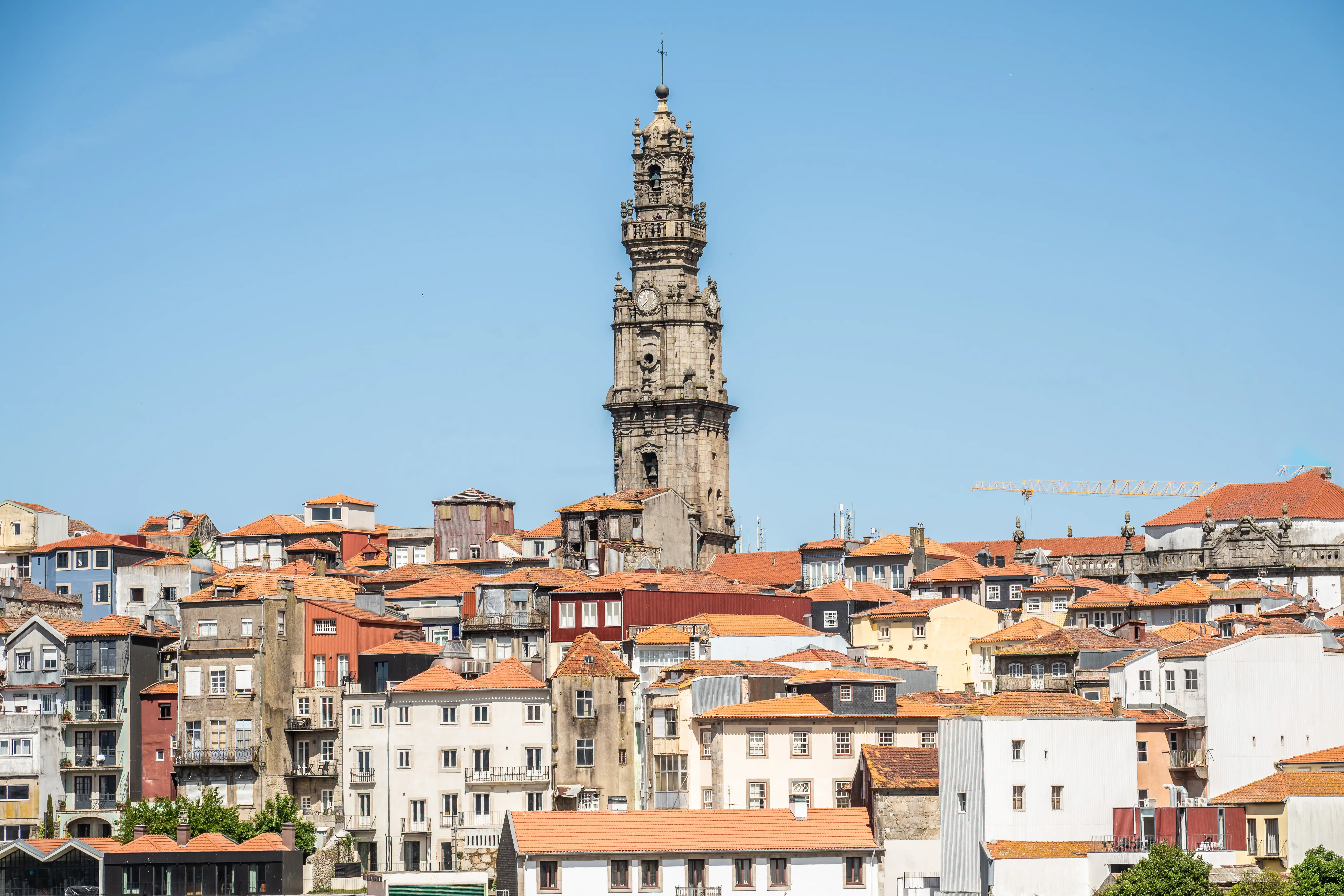 Wide shot of the Clérigos Tower in Porto, Portugal, with many red-tiled roofs and colourful buildings in the foreground, under a bright blue sky