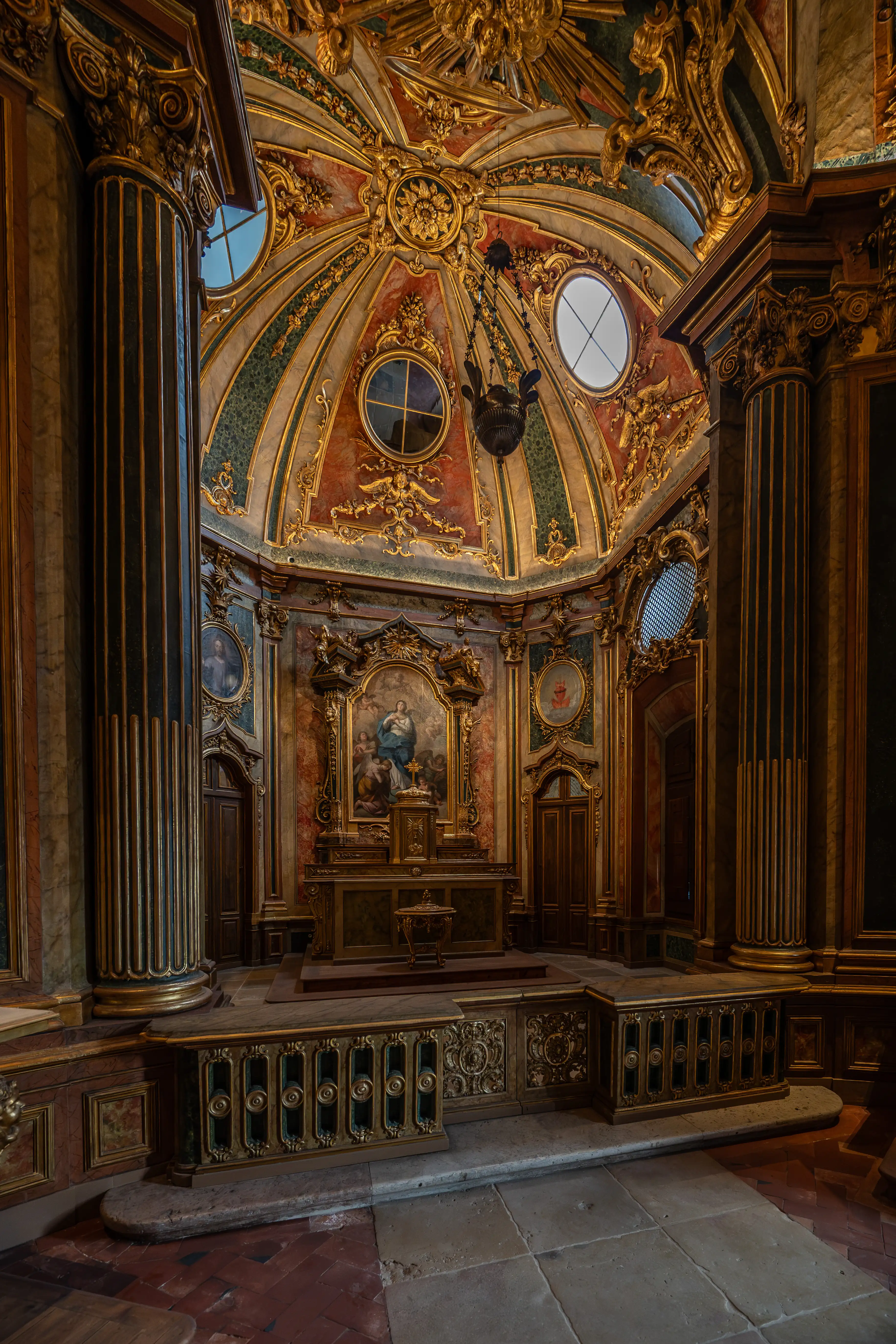 Interior view of a lavishly decorated chapel with a central altar, a domed ceiling adorned with gold and green patterns, and large fluted columns.