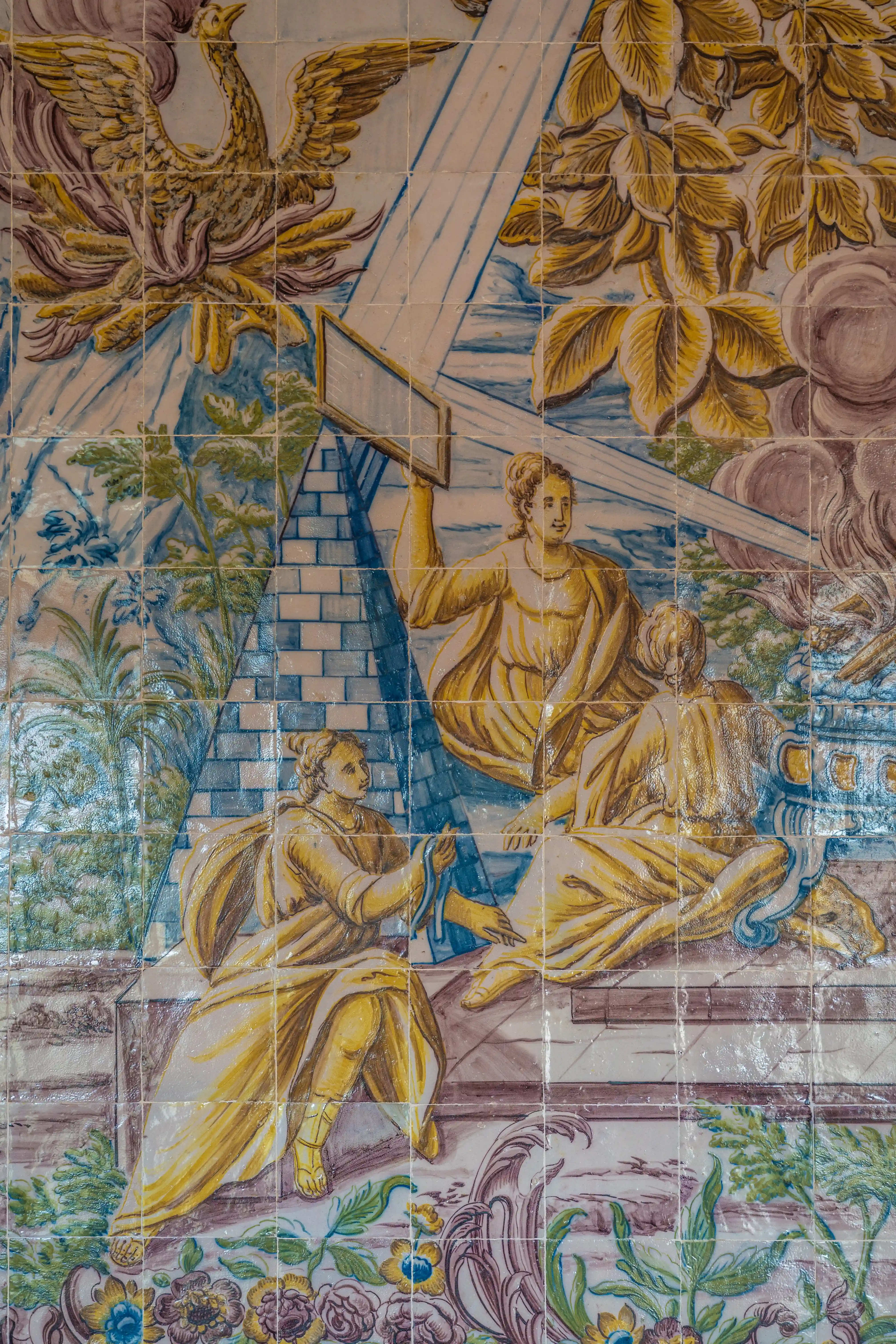Ceramic tile art of a person carrying baskets of fruit on a yoke. The person wears a straw hat and traditional clothing, set against a blue and white landscape with trees and buildings.